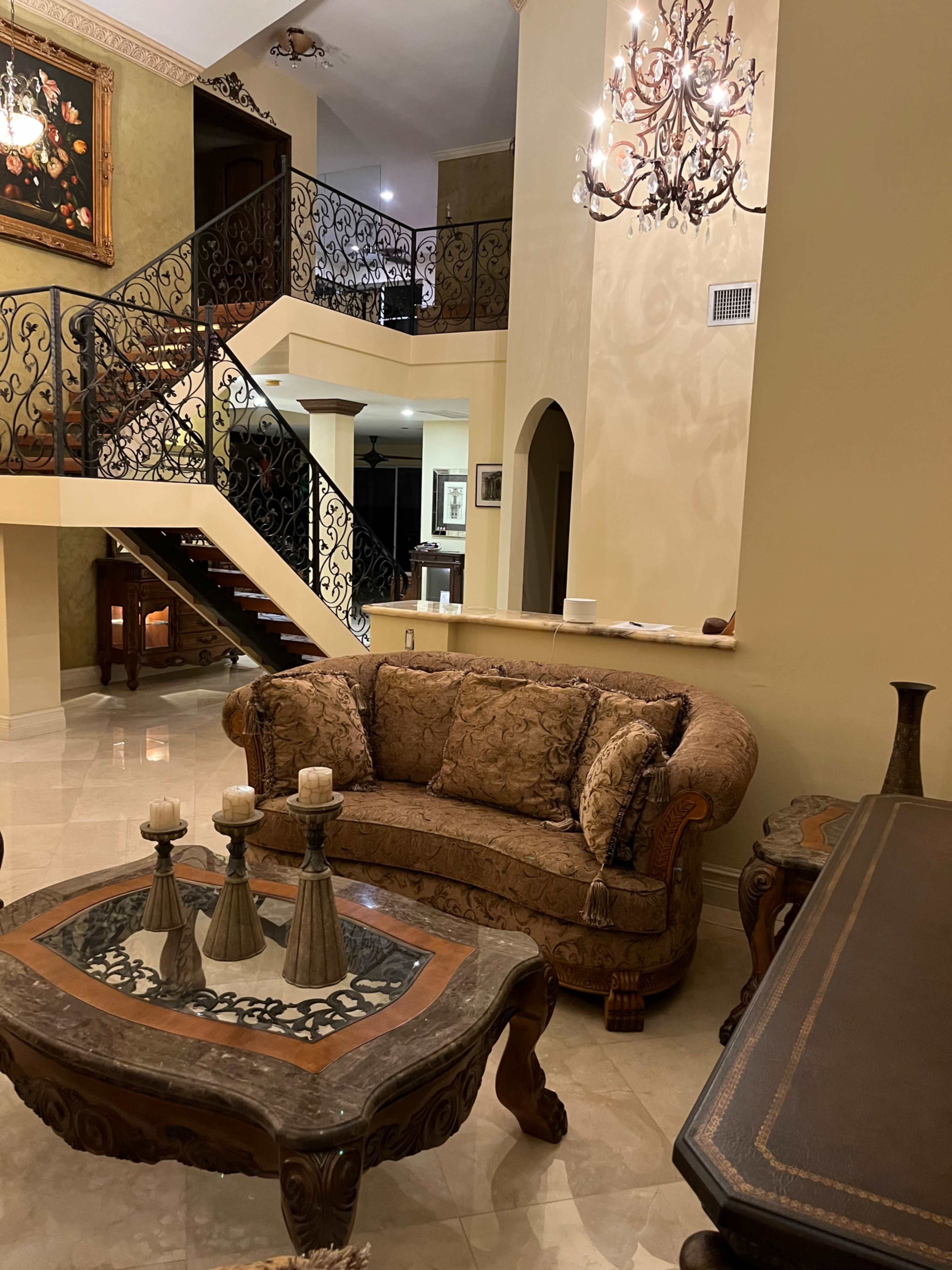 A spacious living room with a patterned sofa, a decorative coffee table, and an elegant chandelier above.