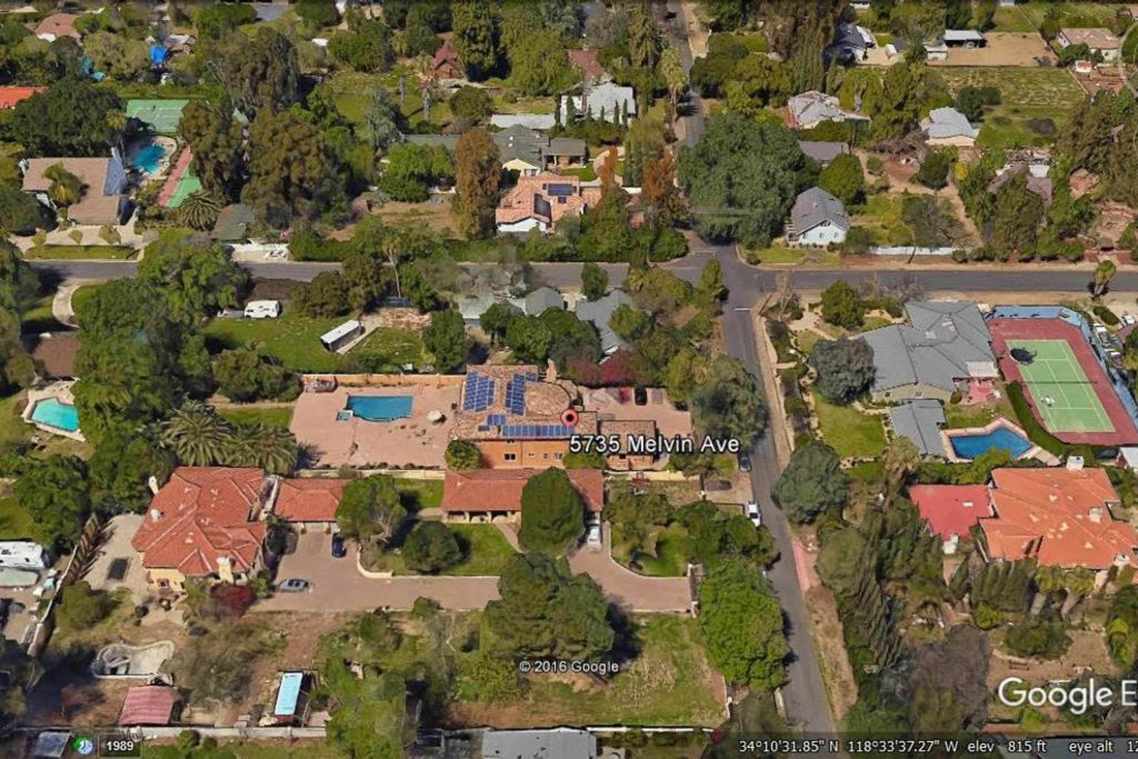 An aerial view of a residential area featuring several houses, swimming pools, and a tennis court.