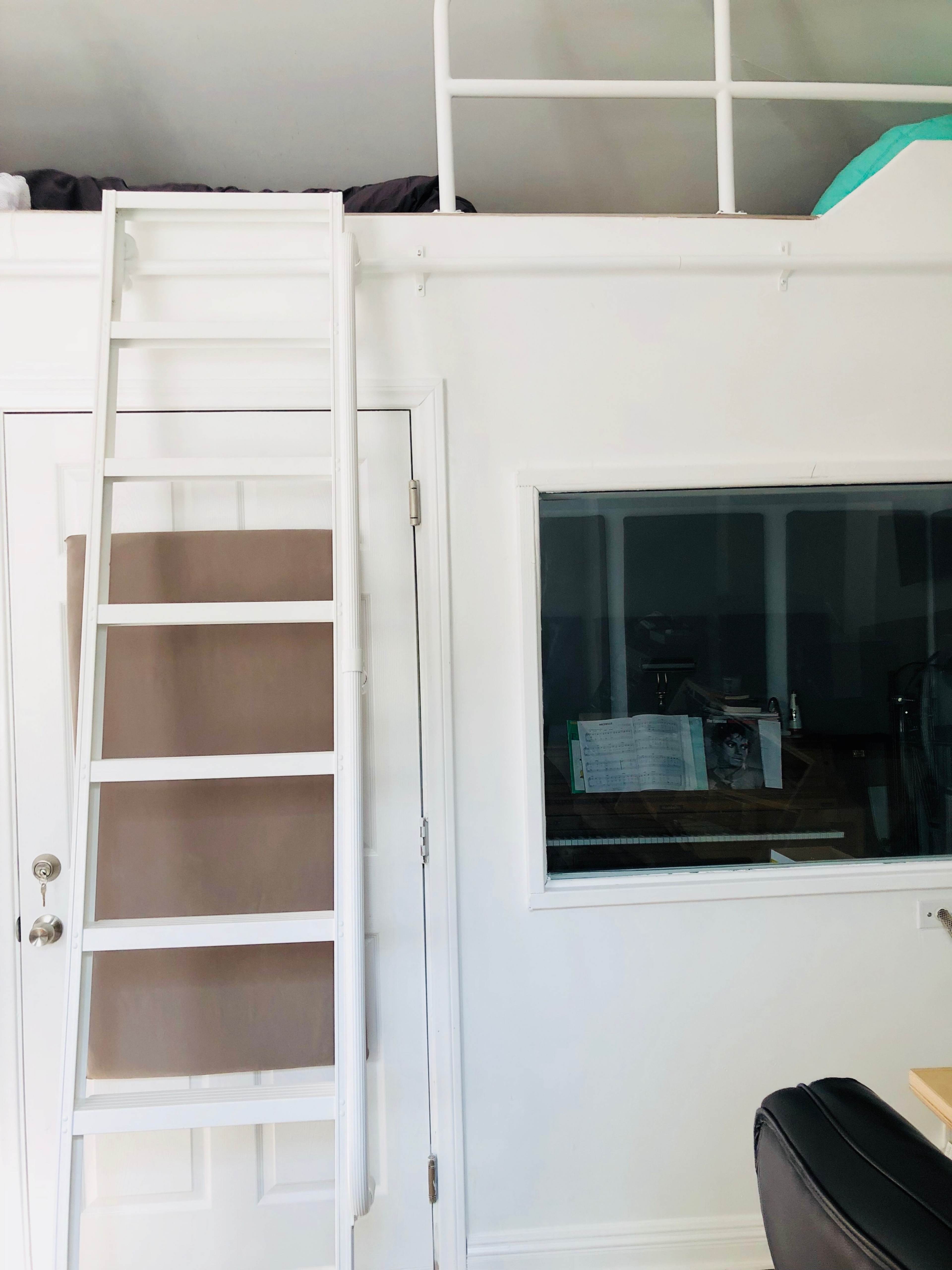 A white room with a lofted bed accessible by a white ladder, along with a door and a window.