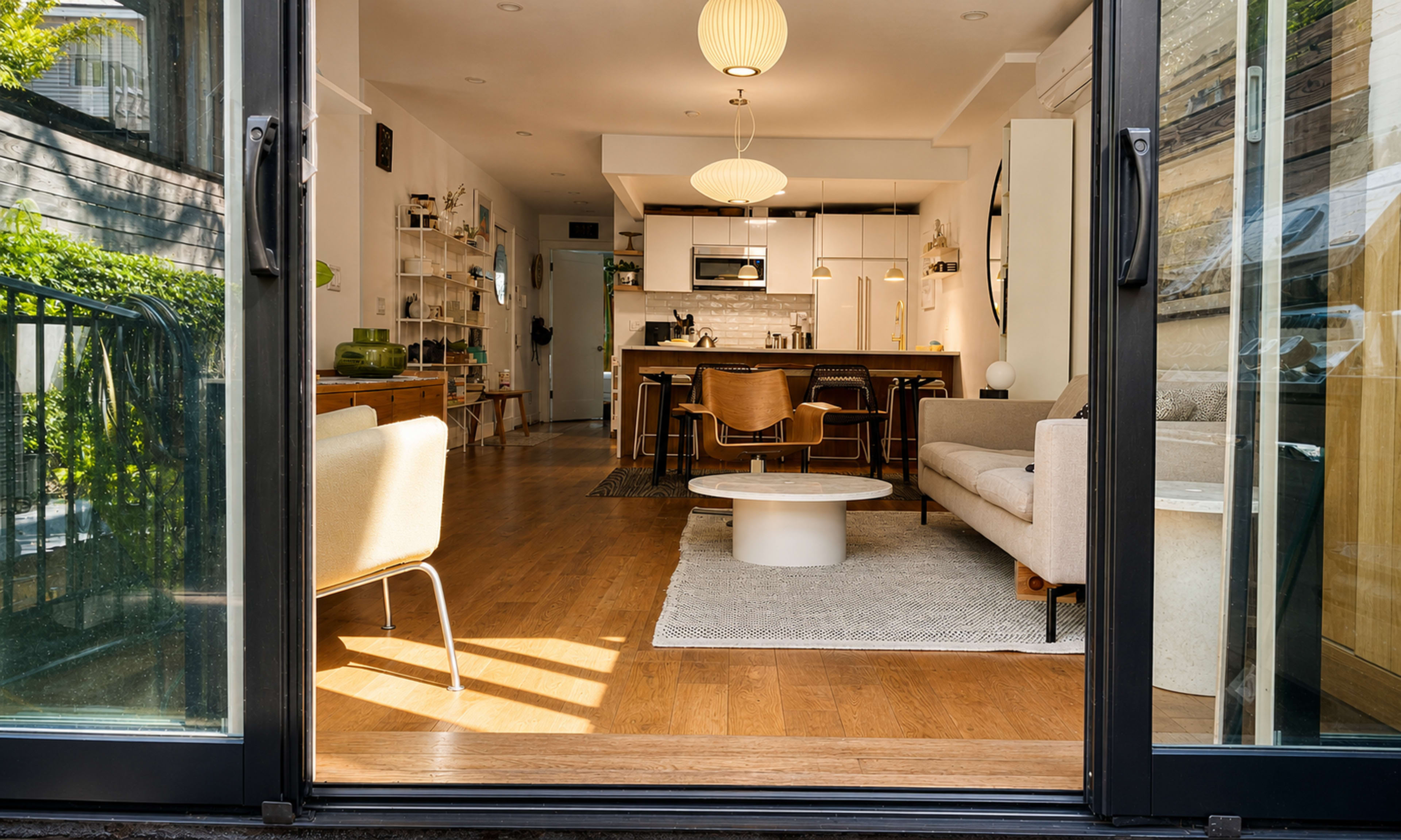 A view from outside shows a modern open-concept living space with a kitchen, dining area, and seating arranged around a circular coffee table.