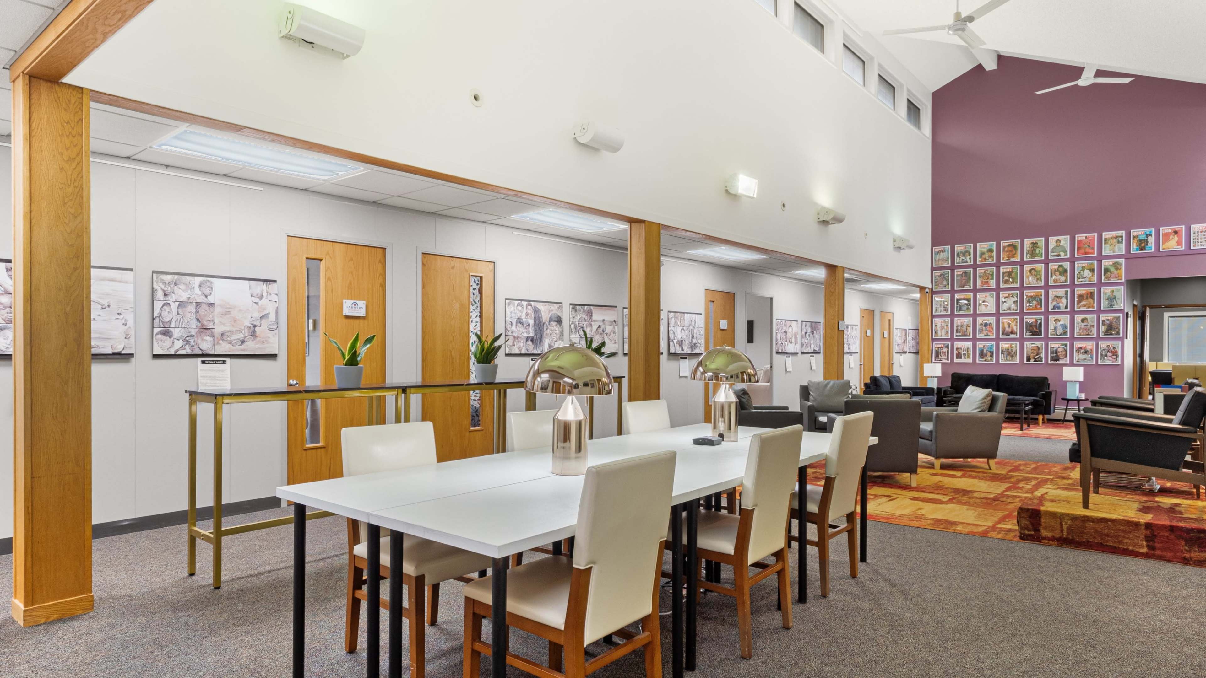 A modern interior space with a large white dining table surrounded by chairs, complemented by a gallery of framed photographs on the walls.