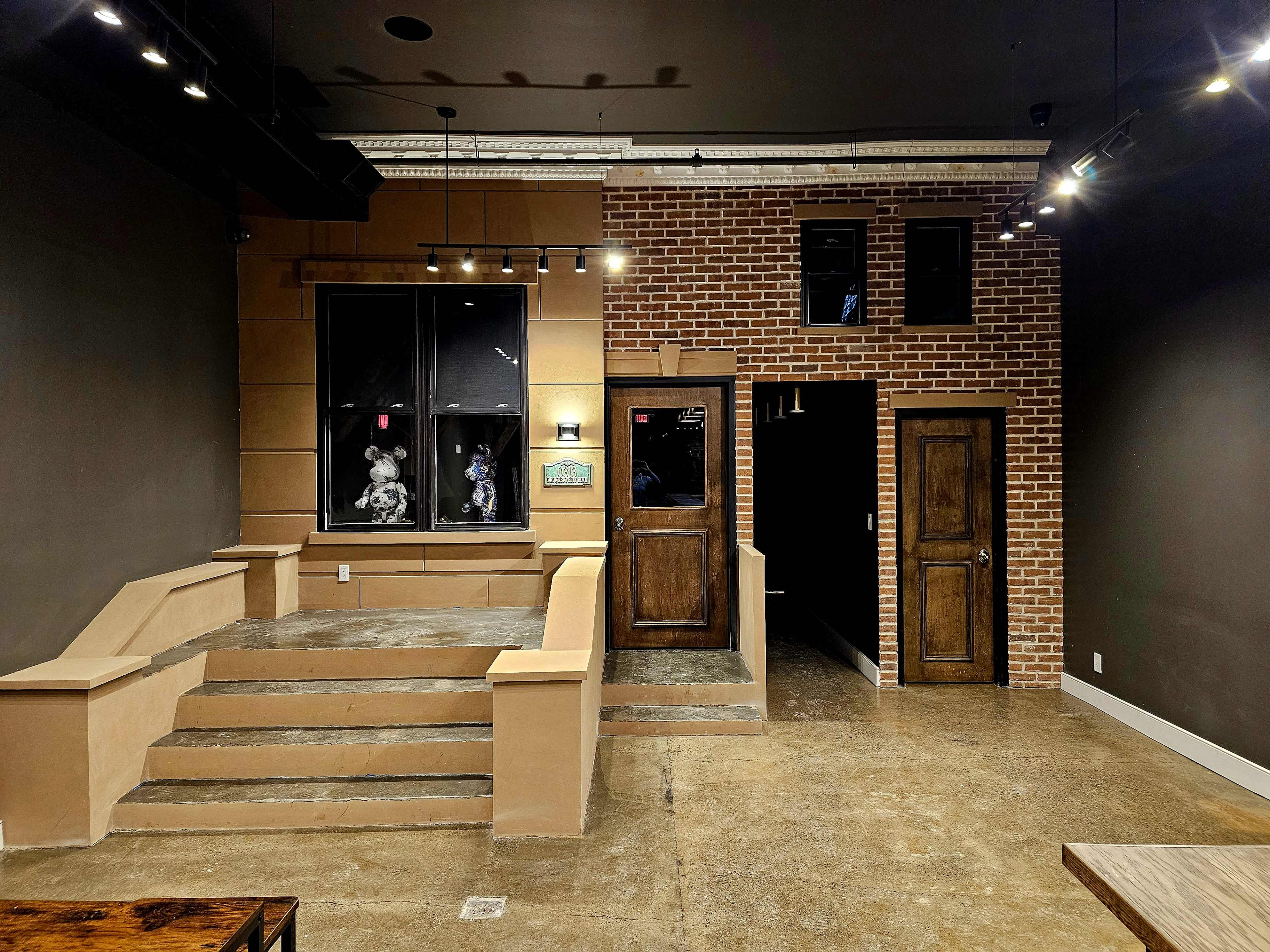 The image shows an interior space featuring a brick wall section with a door, a staircase leading up to a window, and a dark adjacent room.