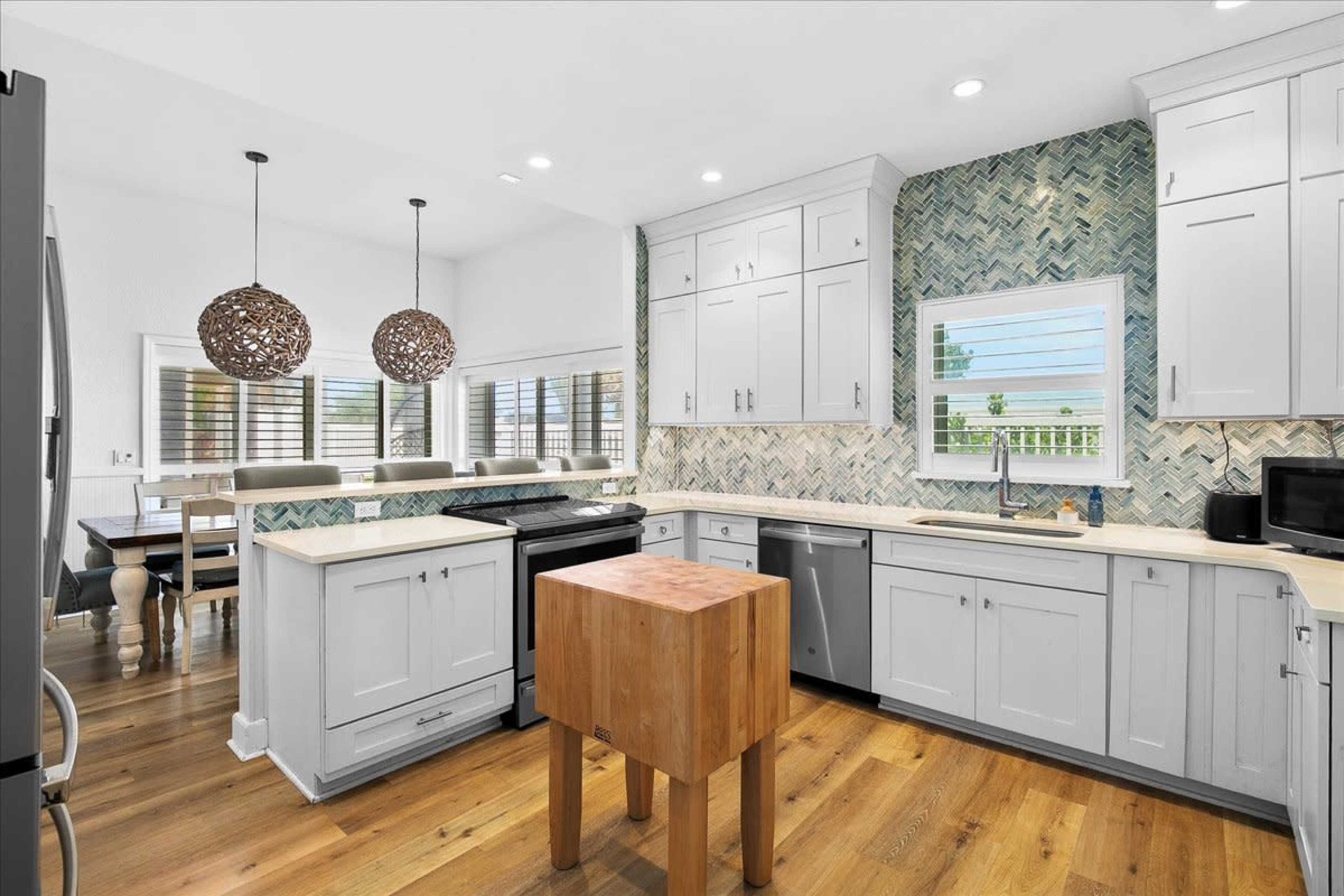 A modern kitchen features white cabinets, a wooden island, and a herringbone-patterned backsplash.