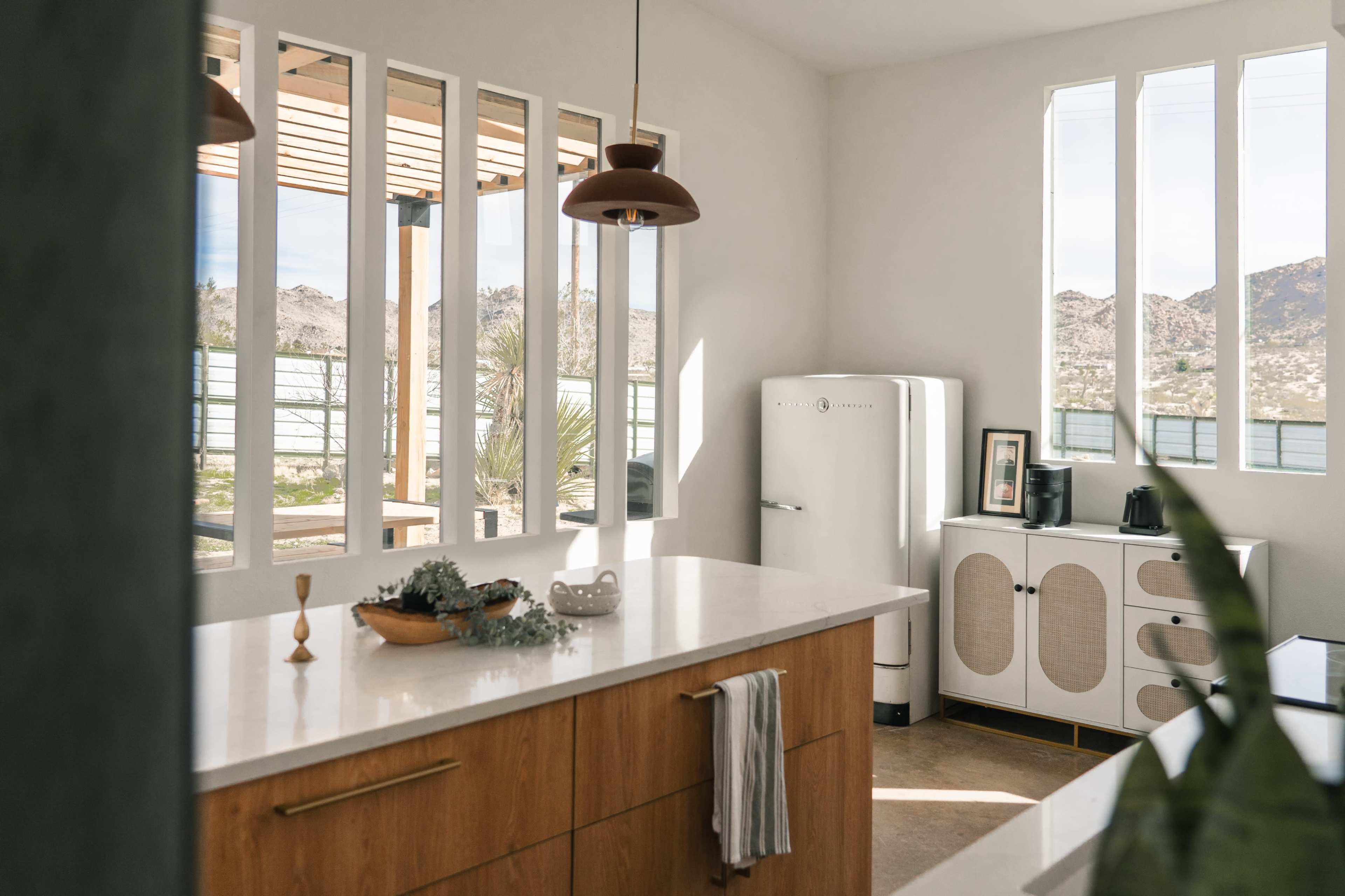 A modern kitchen features a wooden island, vintage refrigerator, and large windows overlooking a desert landscape.
