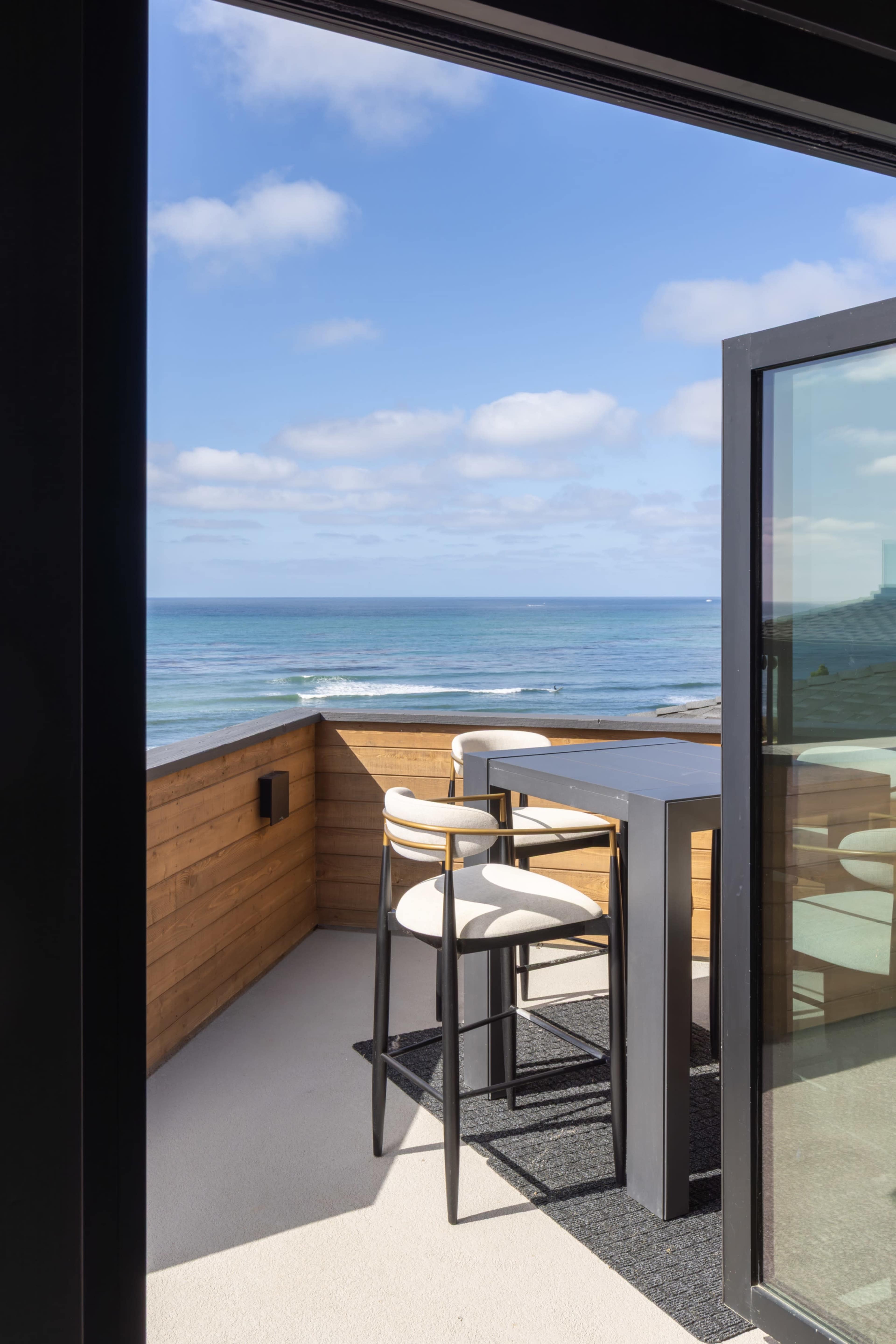 A balcony features a high table and stools overlooking the ocean with a clear sky.
