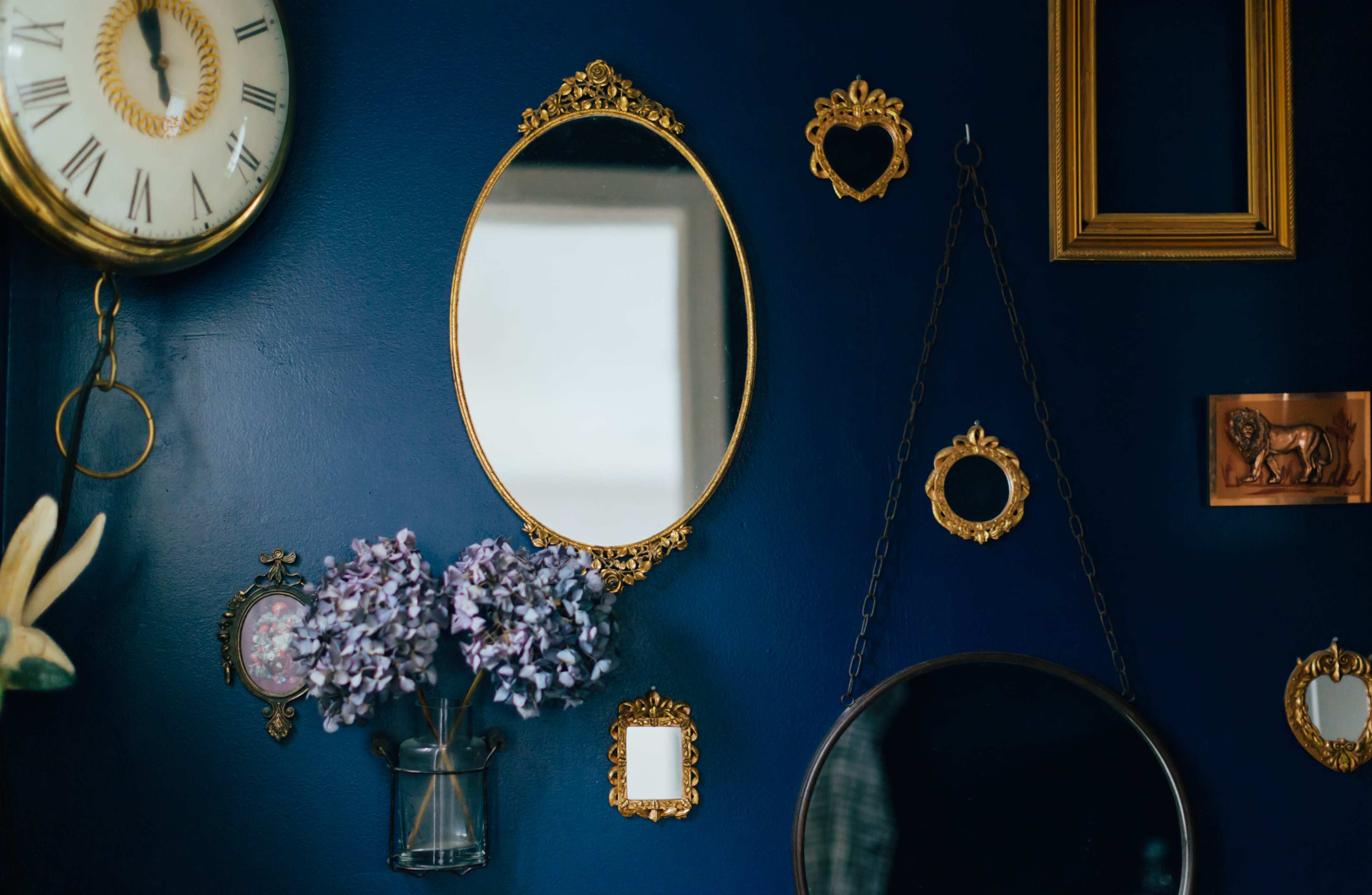 A dark blue wall adorned with various ornate mirrors, a clock, and decorative floral arrangements.