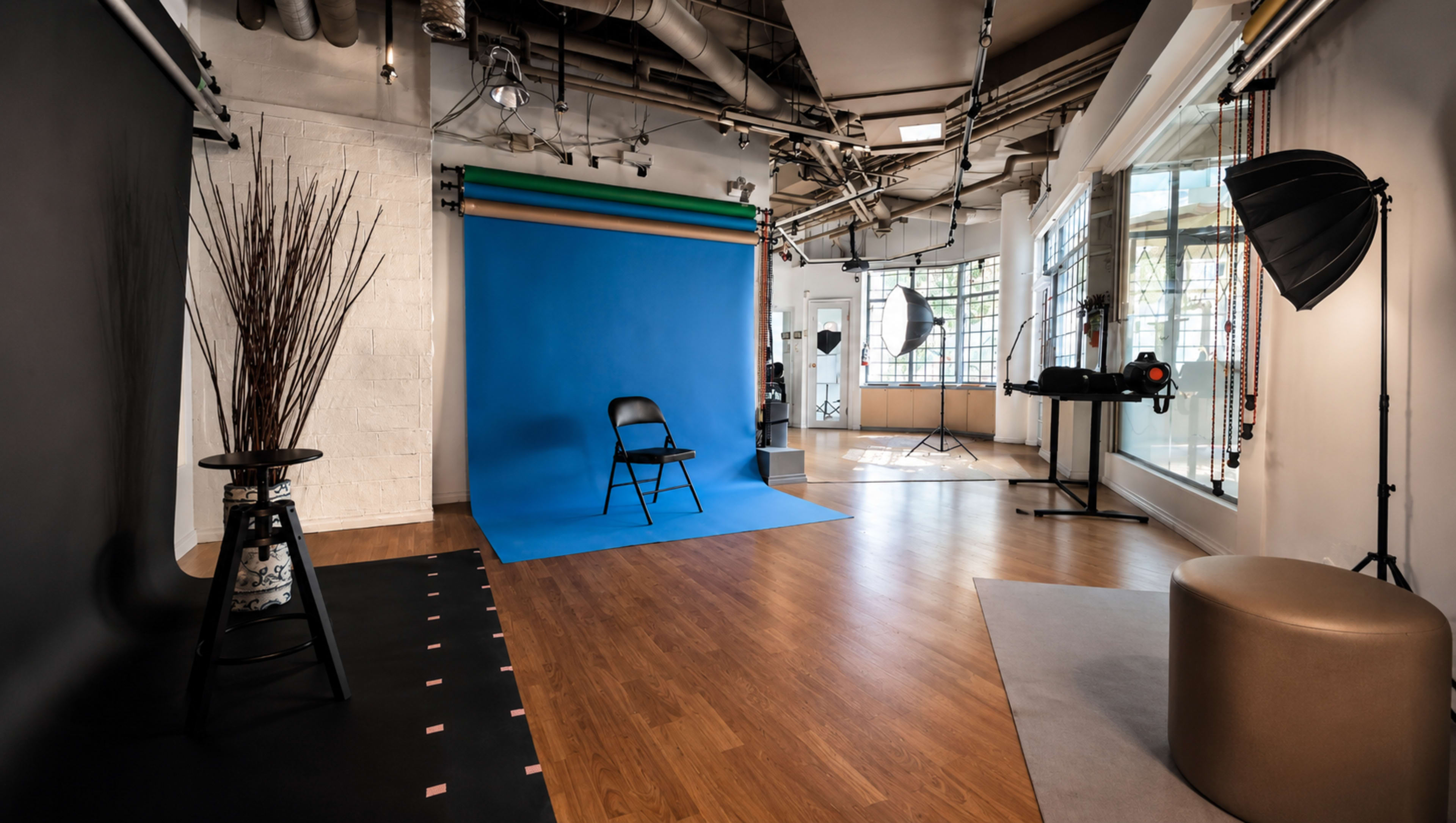 The image shows a photography studio featuring a blue backdrop, a black chair, and various lighting equipment arranged throughout the space.