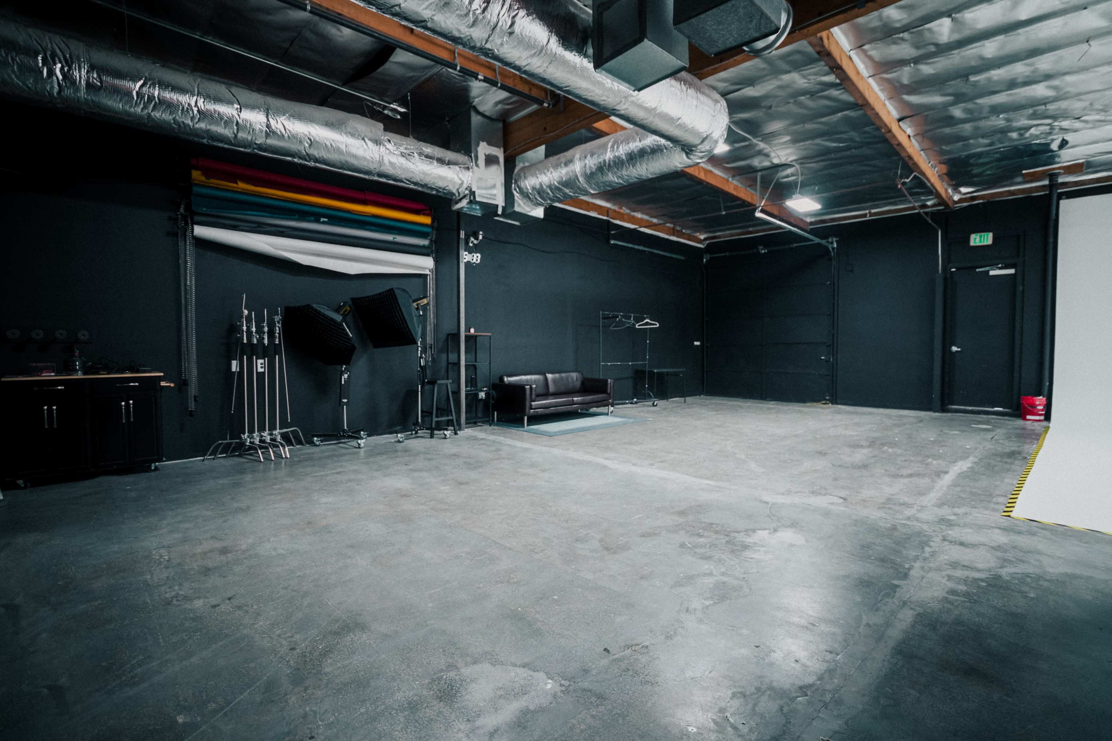 An empty studio space with a dark background, a black couch, and various equipment stands along one side.