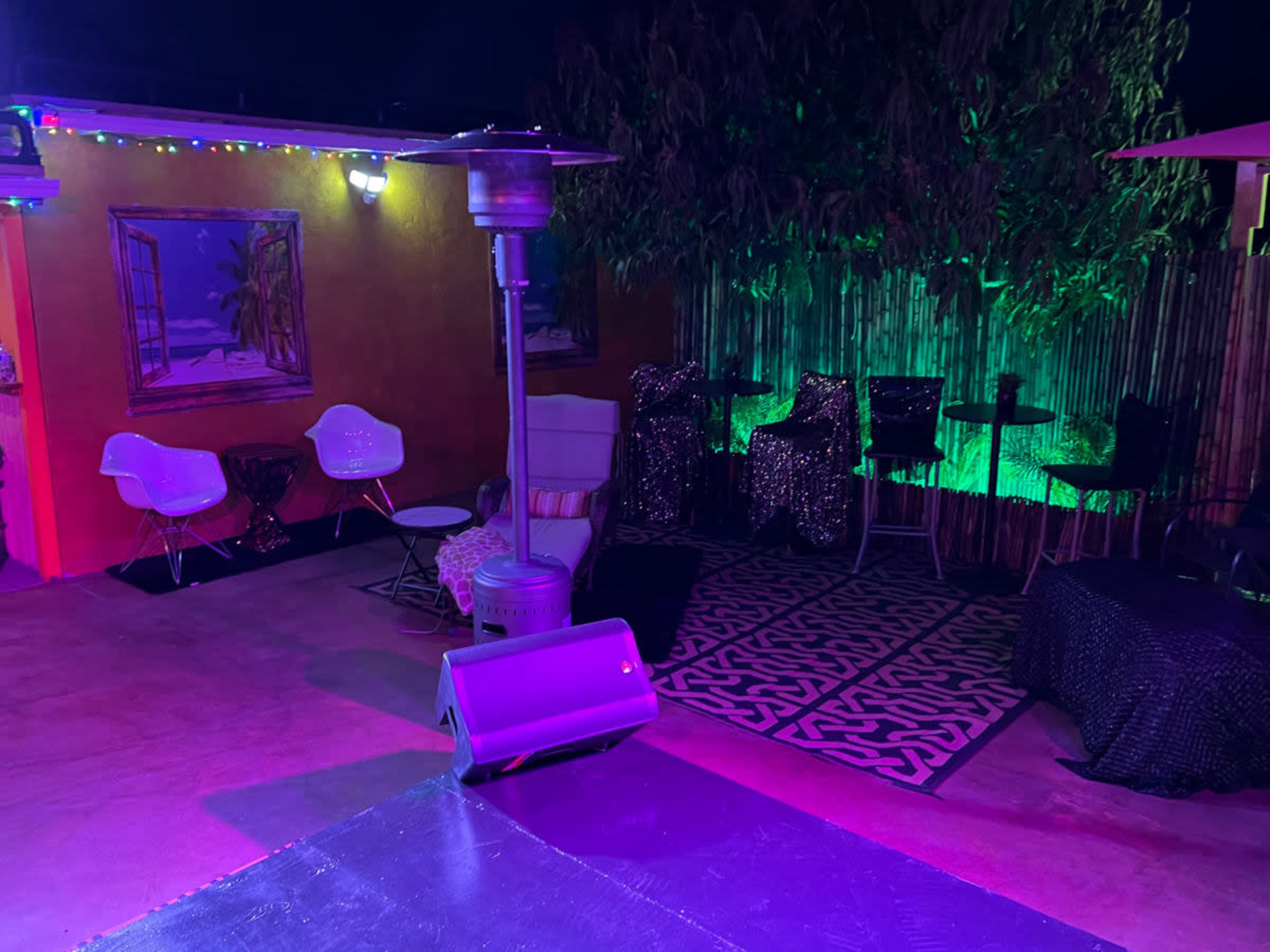 The scene shows a colorful outdoor seating area with patio heaters, various chairs, and decorated walls under nighttime lighting.