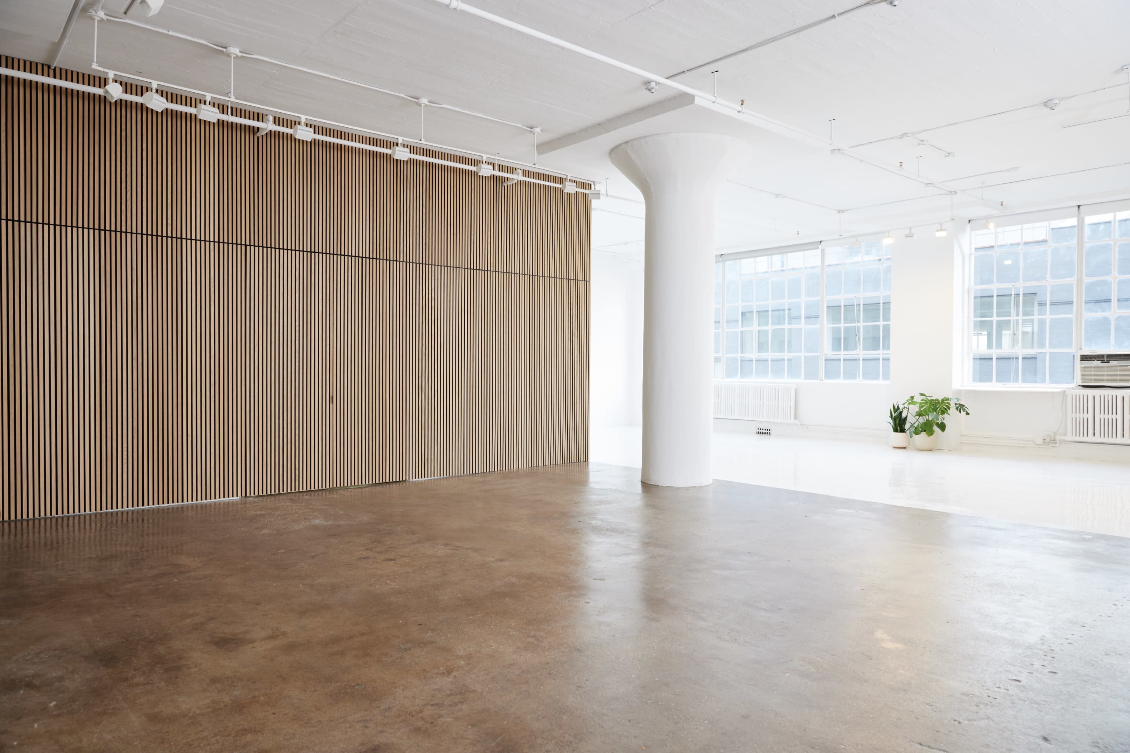 A spacious, minimalist interior with wooden paneling on one wall and large windows allowing natural light to fill the room.