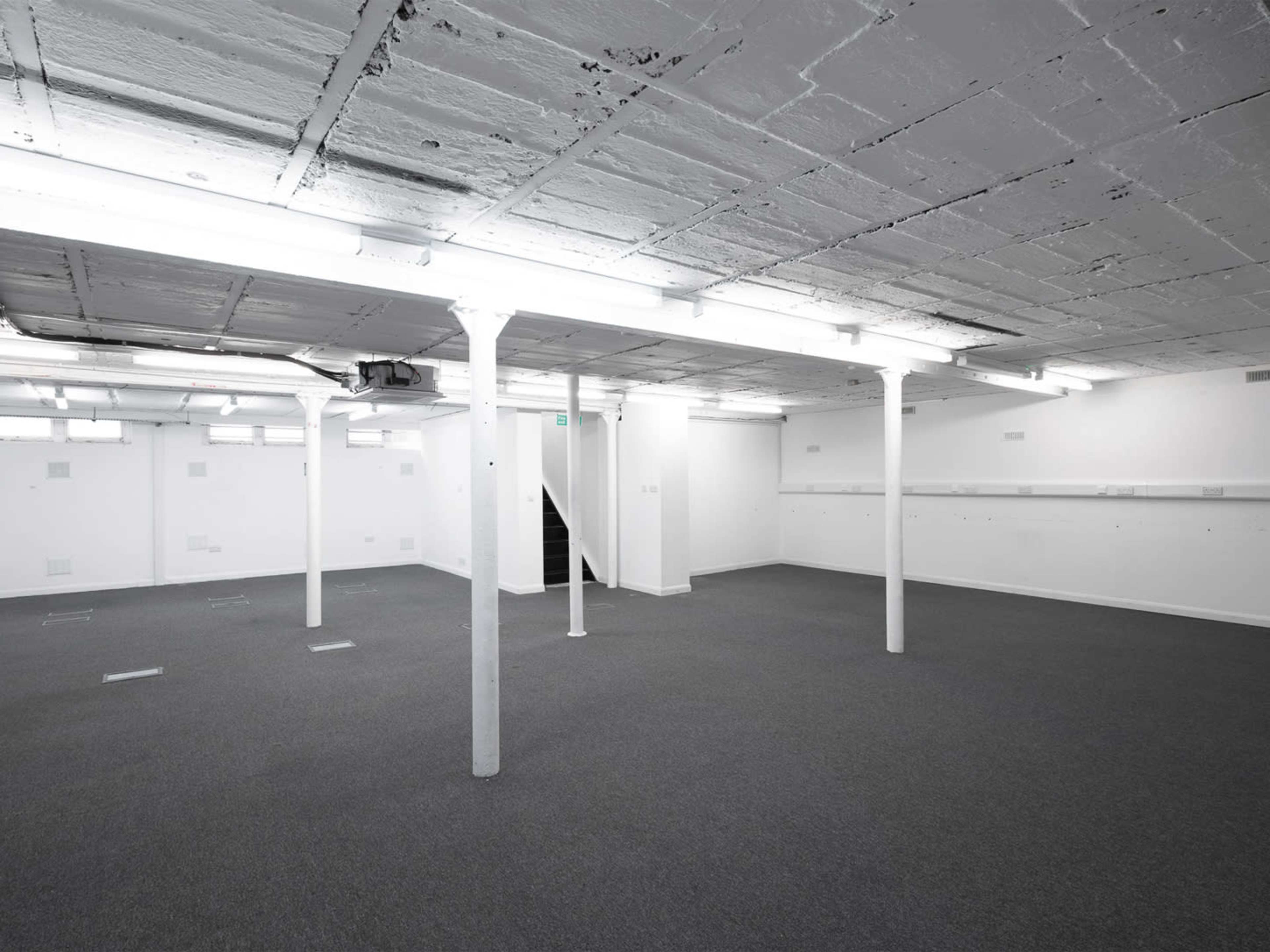 The image shows a spacious, empty basement with concrete pillars and bright overhead lighting.