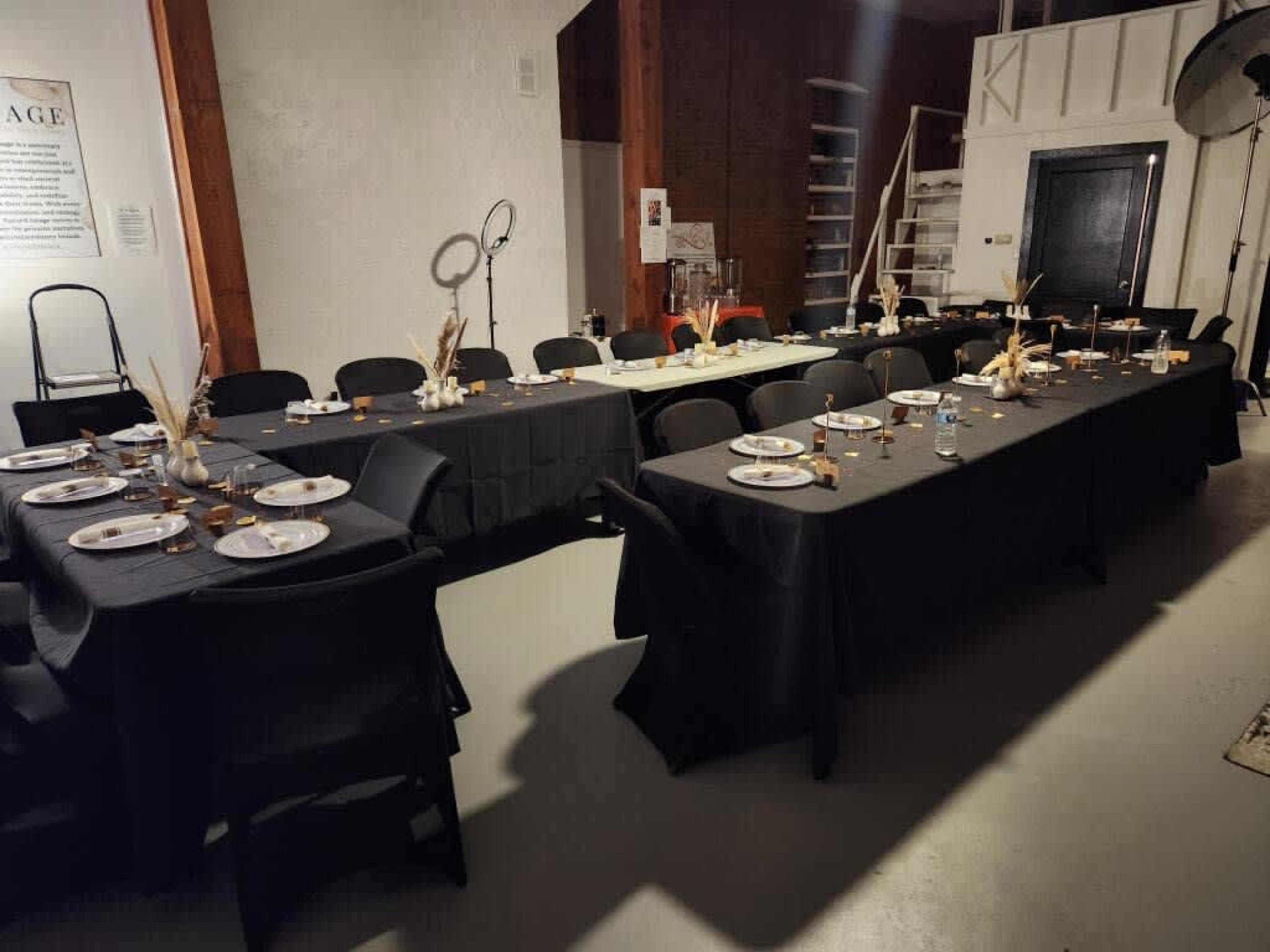 A spacious dining area features several long tables covered with black tablecloths, set with plates and decorative centerpieces.