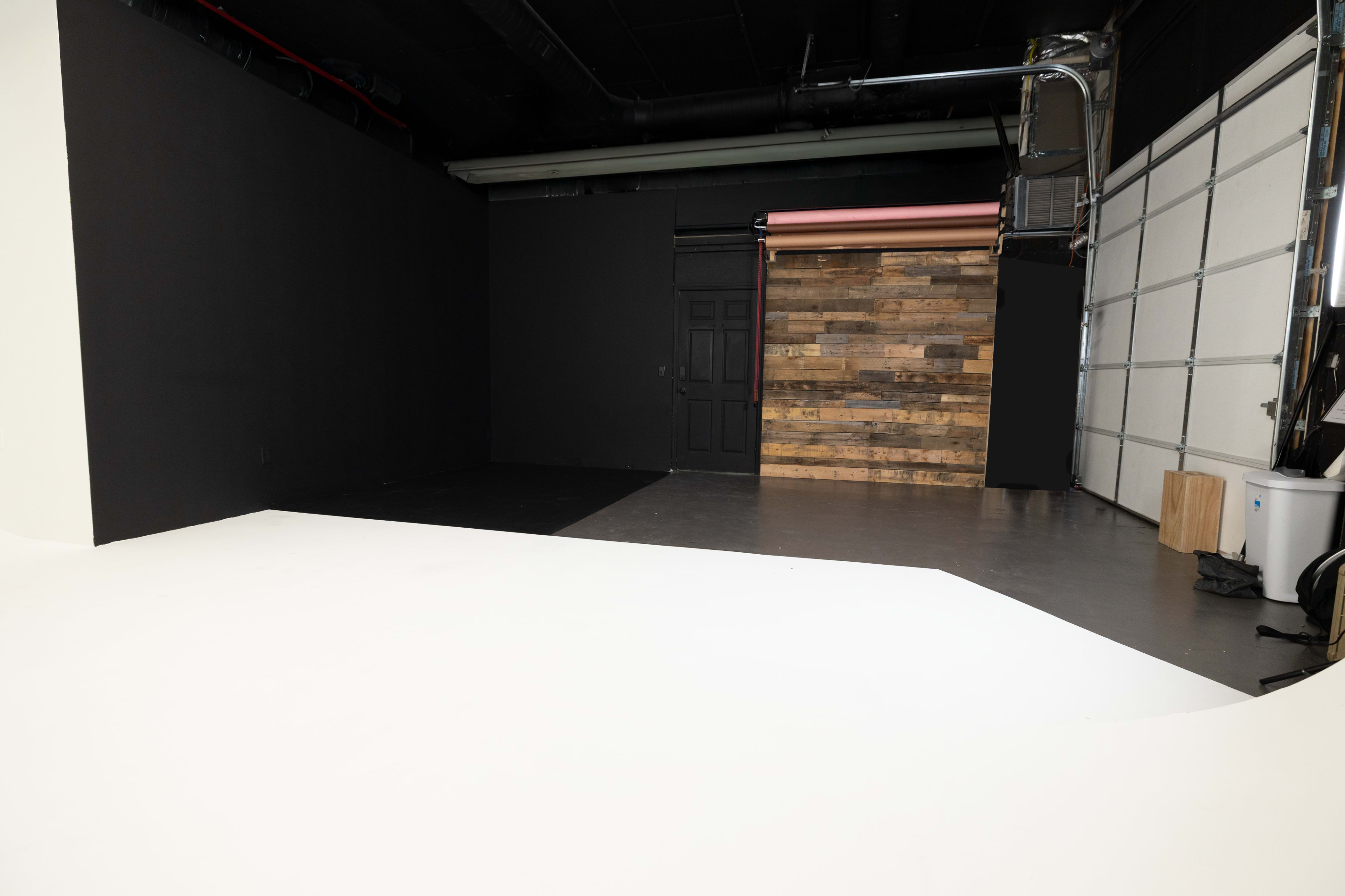 The image shows a photography studio featuring a black wall, a wood-paneled section, and a white floor.