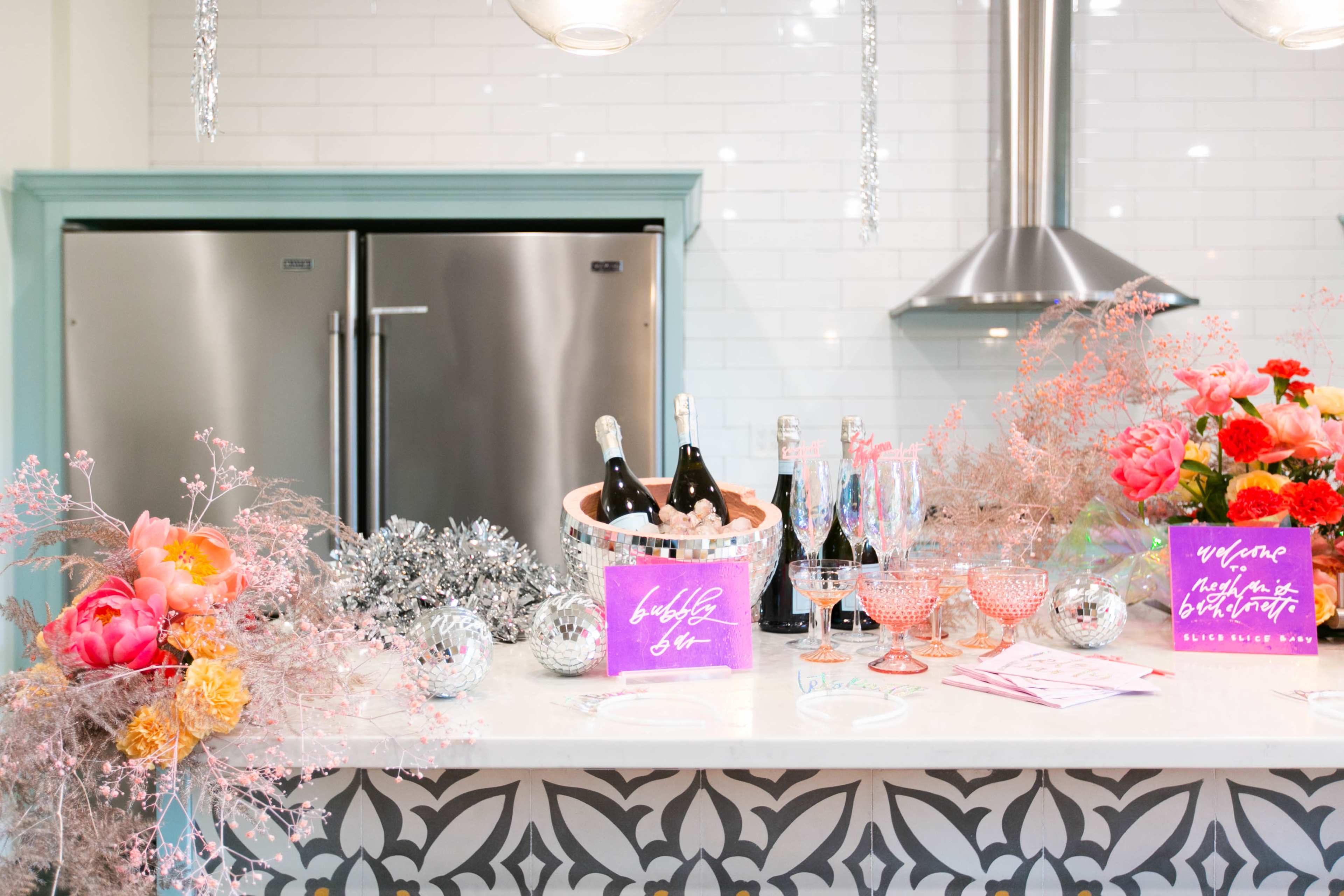 A festive kitchen countertop is adorned with champagne bottles, colorful floral arrangements, and decorative signs for a celebration.