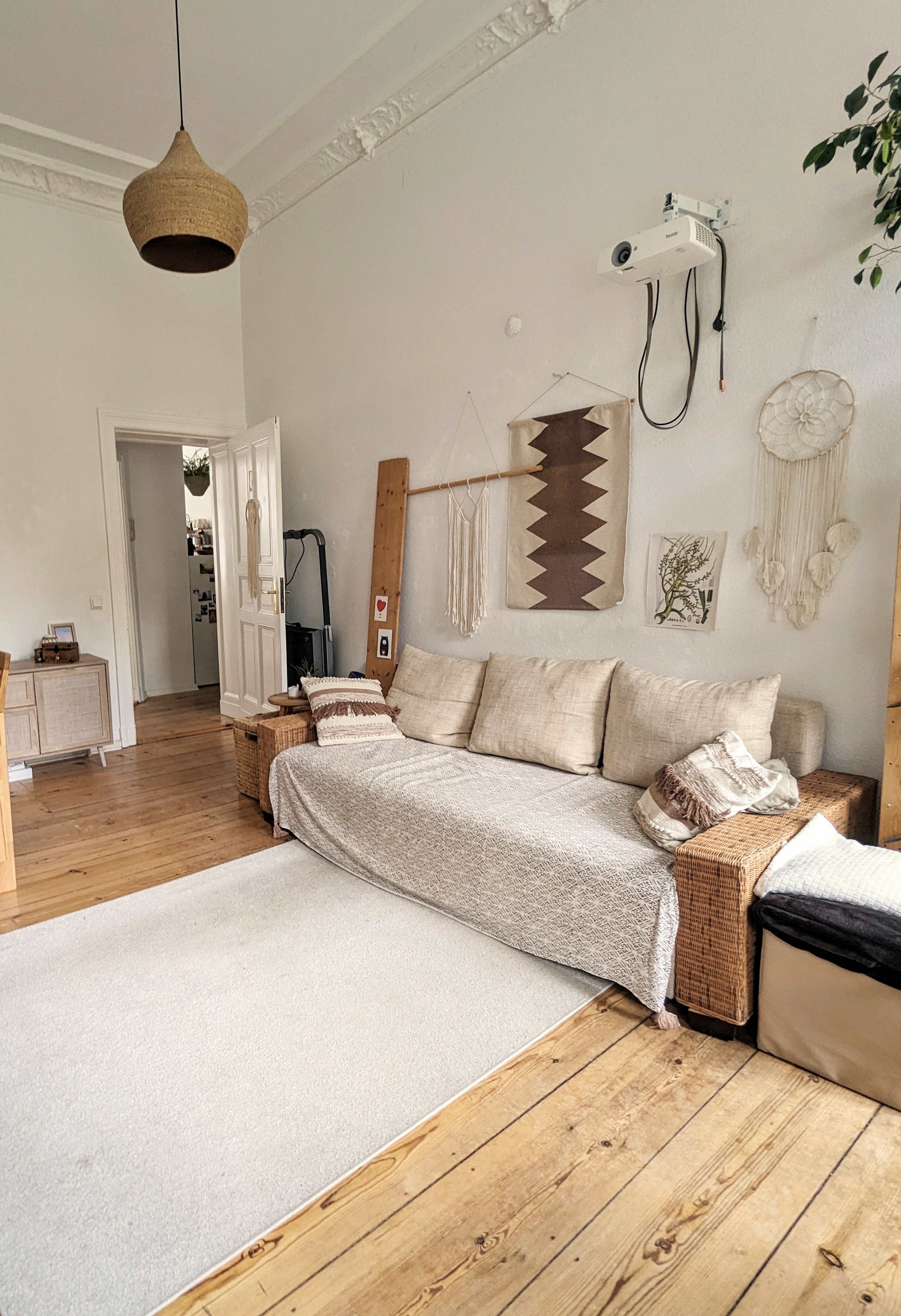 A living room with a light-colored sofa covered by a throw, wooden floorboards, and decorative wall hangings.