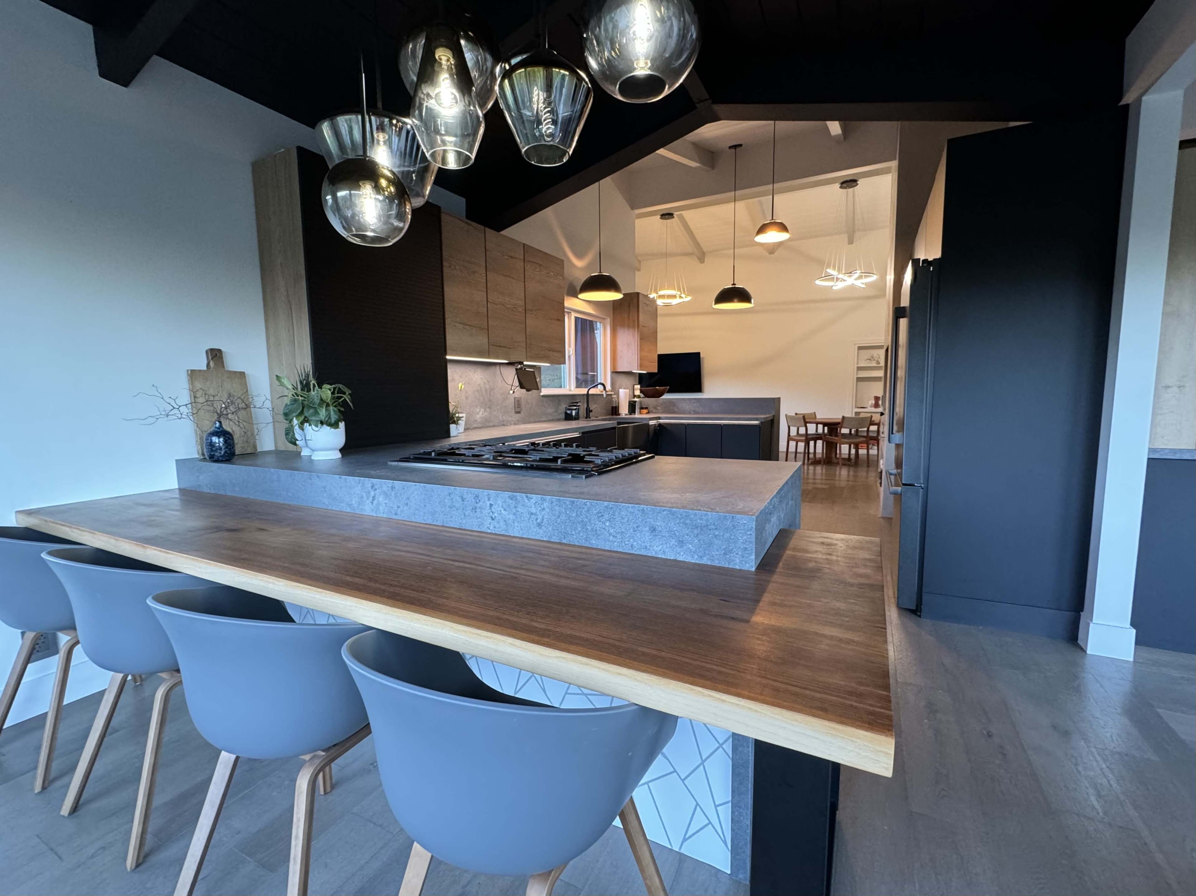 A modern kitchen with a central island featuring a cooktop and grey bar stools, illuminated by hanging pendant lights.