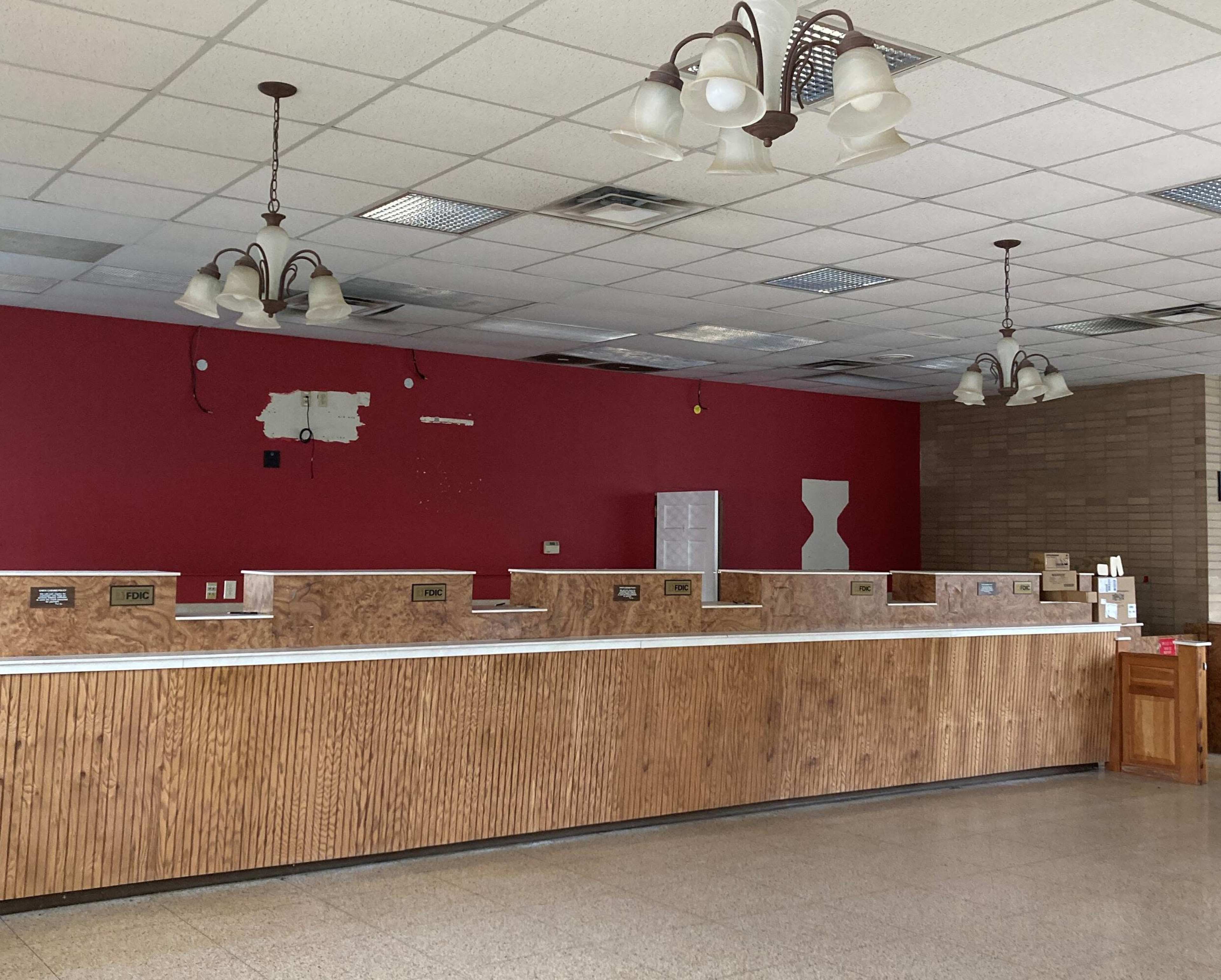 An empty reception area with a wooden counter, several light fixtures, and a red wall in the background.