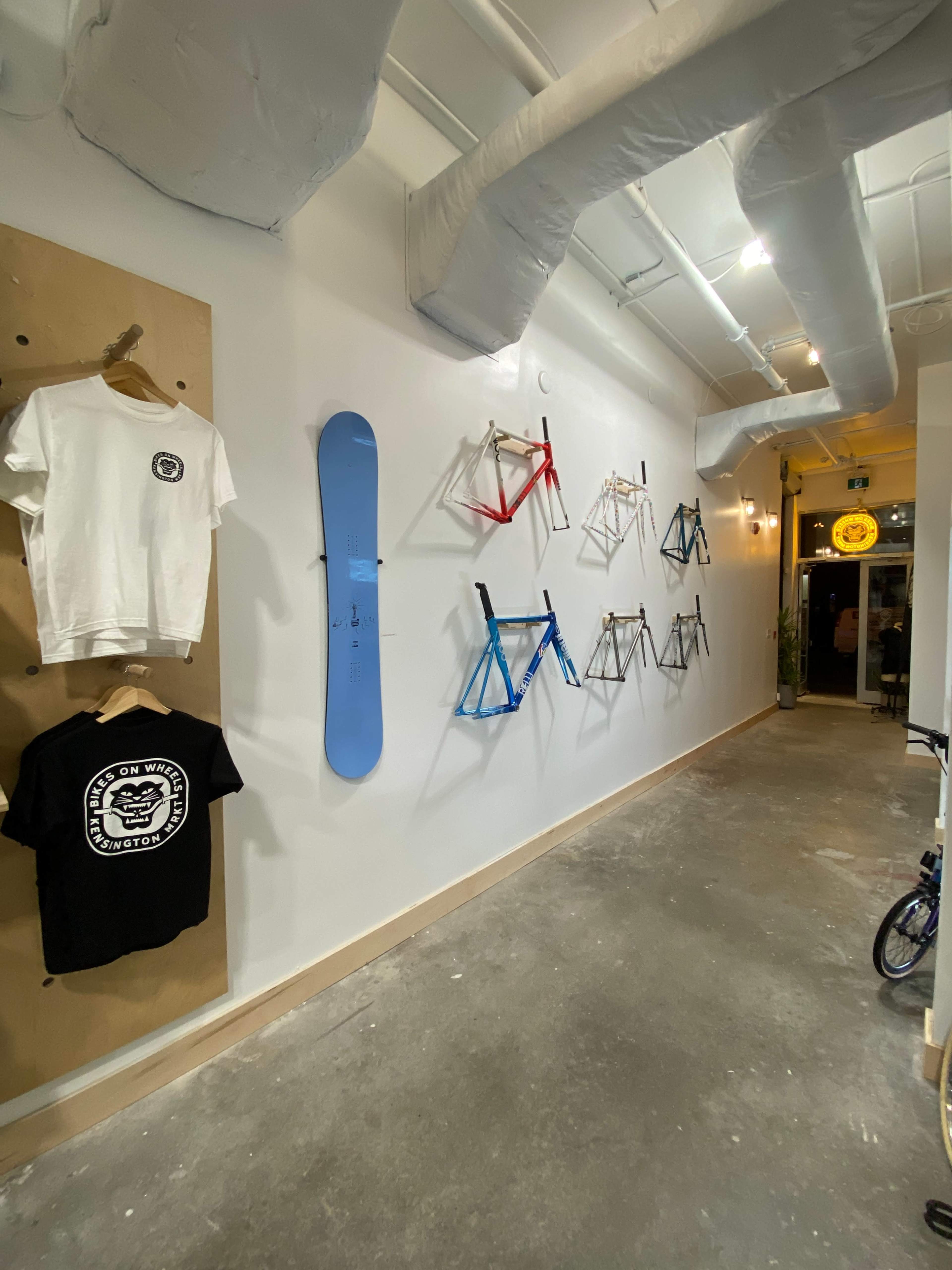 The image shows a hallway with a clothing display on the left and various bicycle frames mounted on the wall to the right, leading to an entrance at the far end.