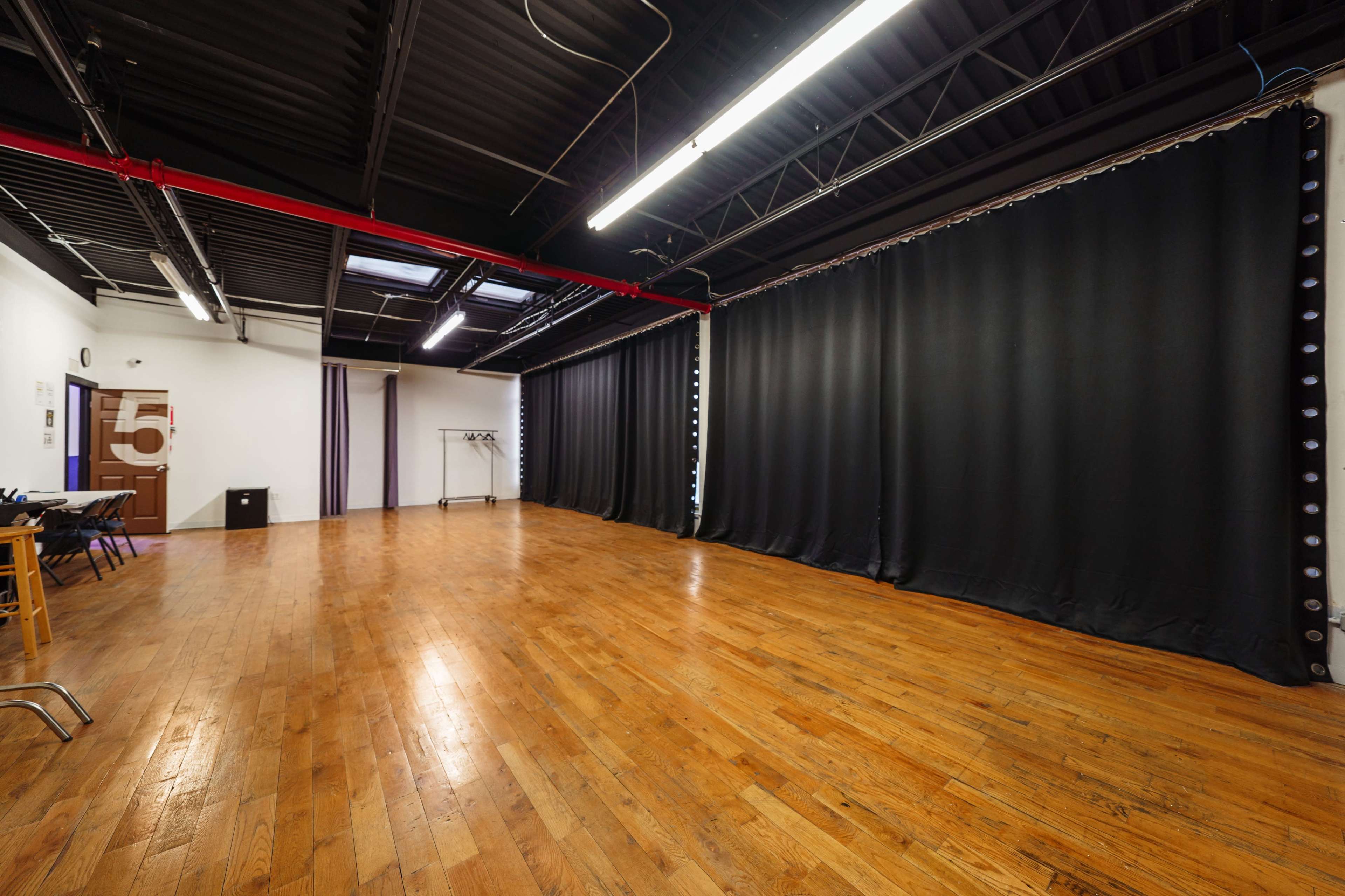 A large, empty studio space with wooden floors and black curtains along one wall.