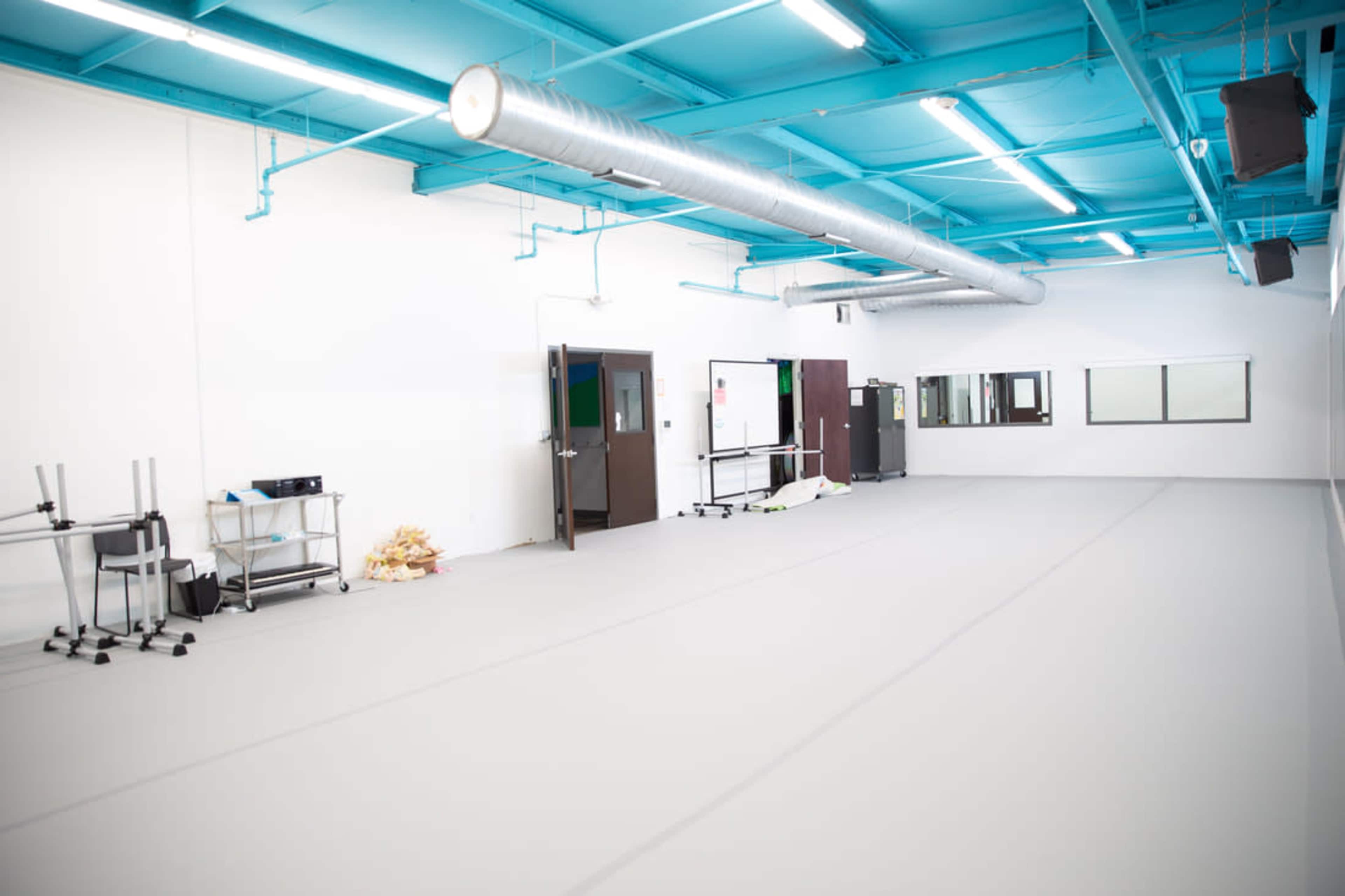 A spacious, empty room with gray flooring and bright blue ceiling beams.
