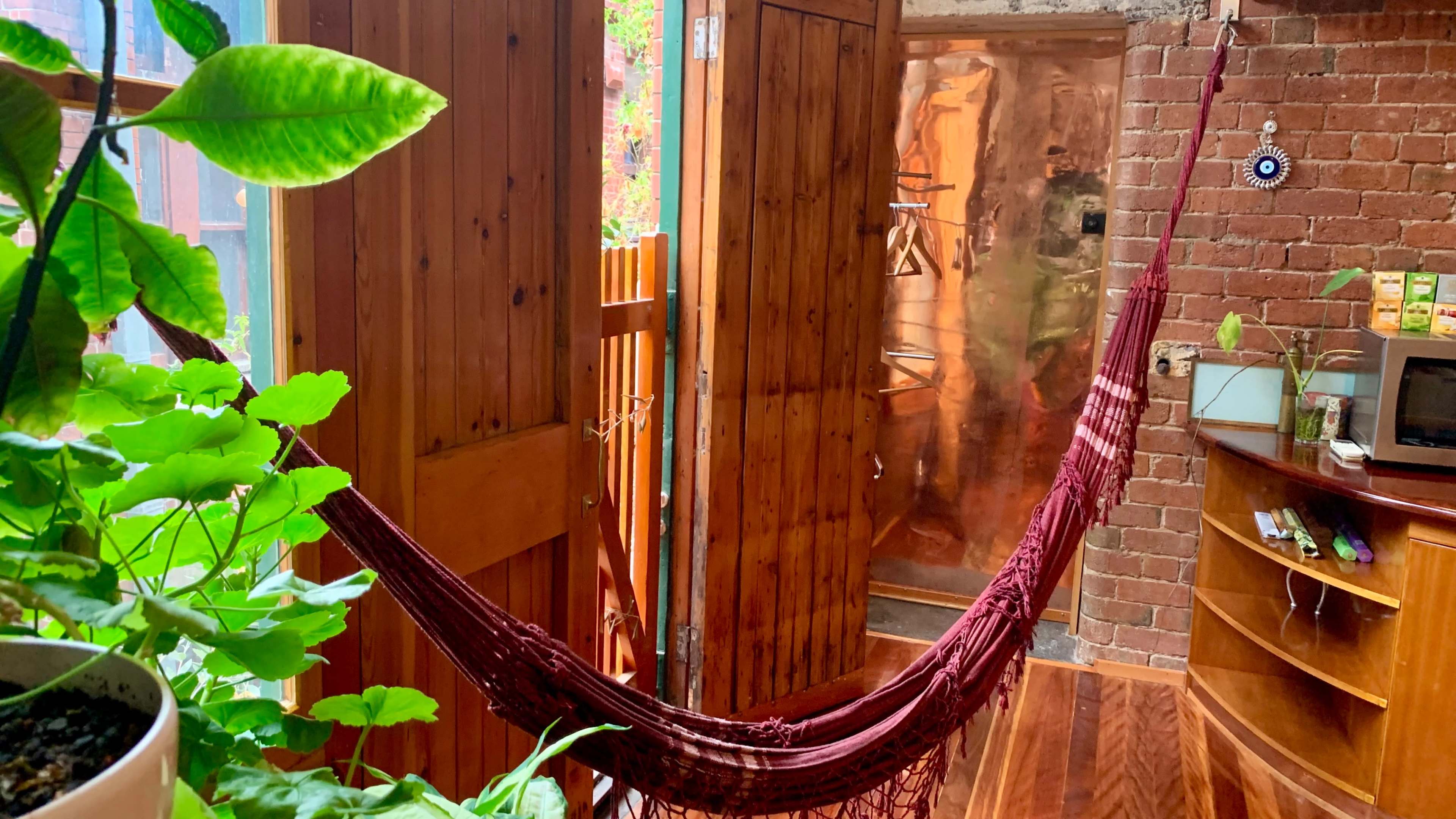 A hammock hangs between wooden doors in a room adorned with plants and exposed brick walls.