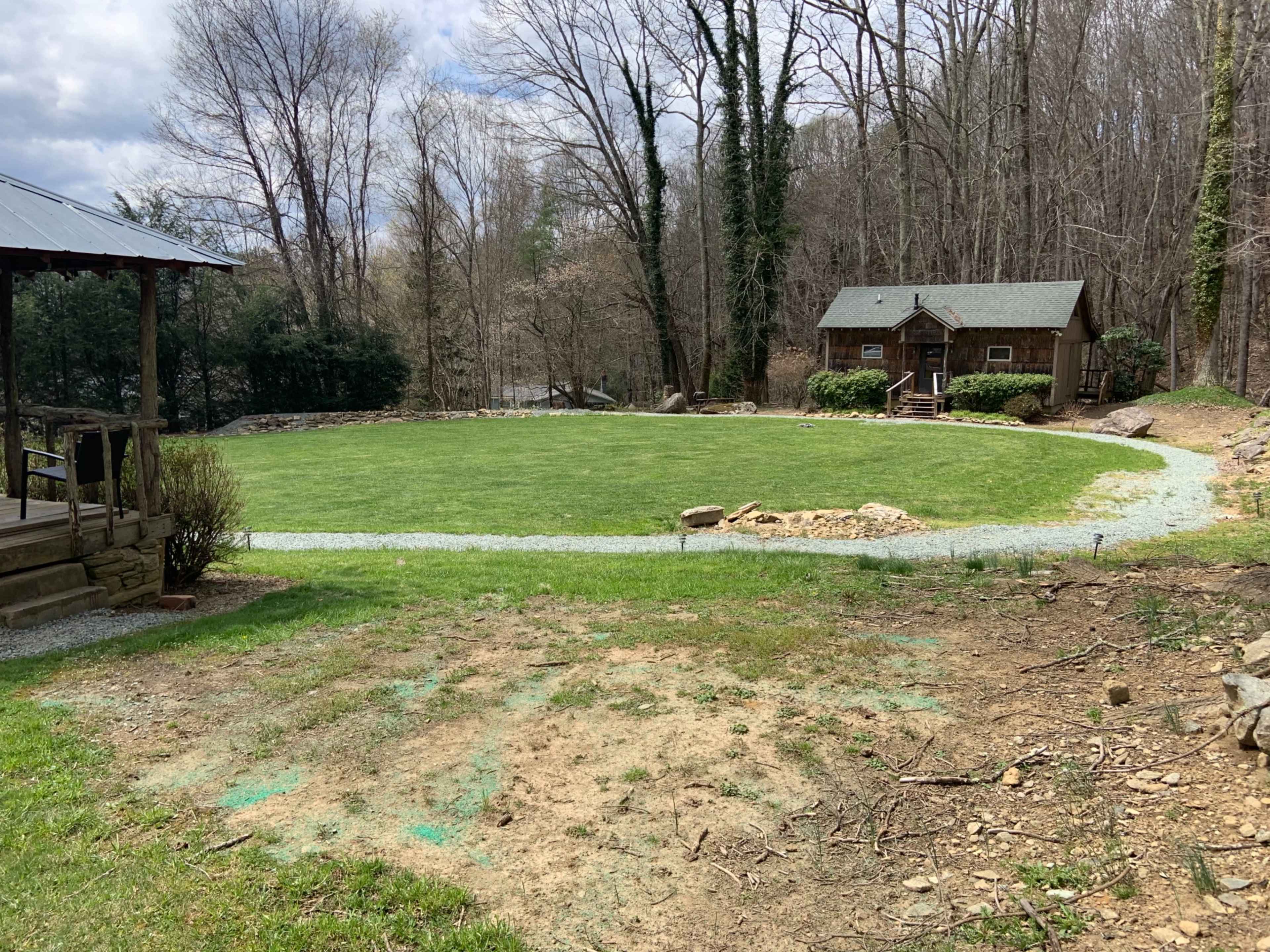 A grassy clearing with a gravel path leads to a wooden cabin surrounded by trees.