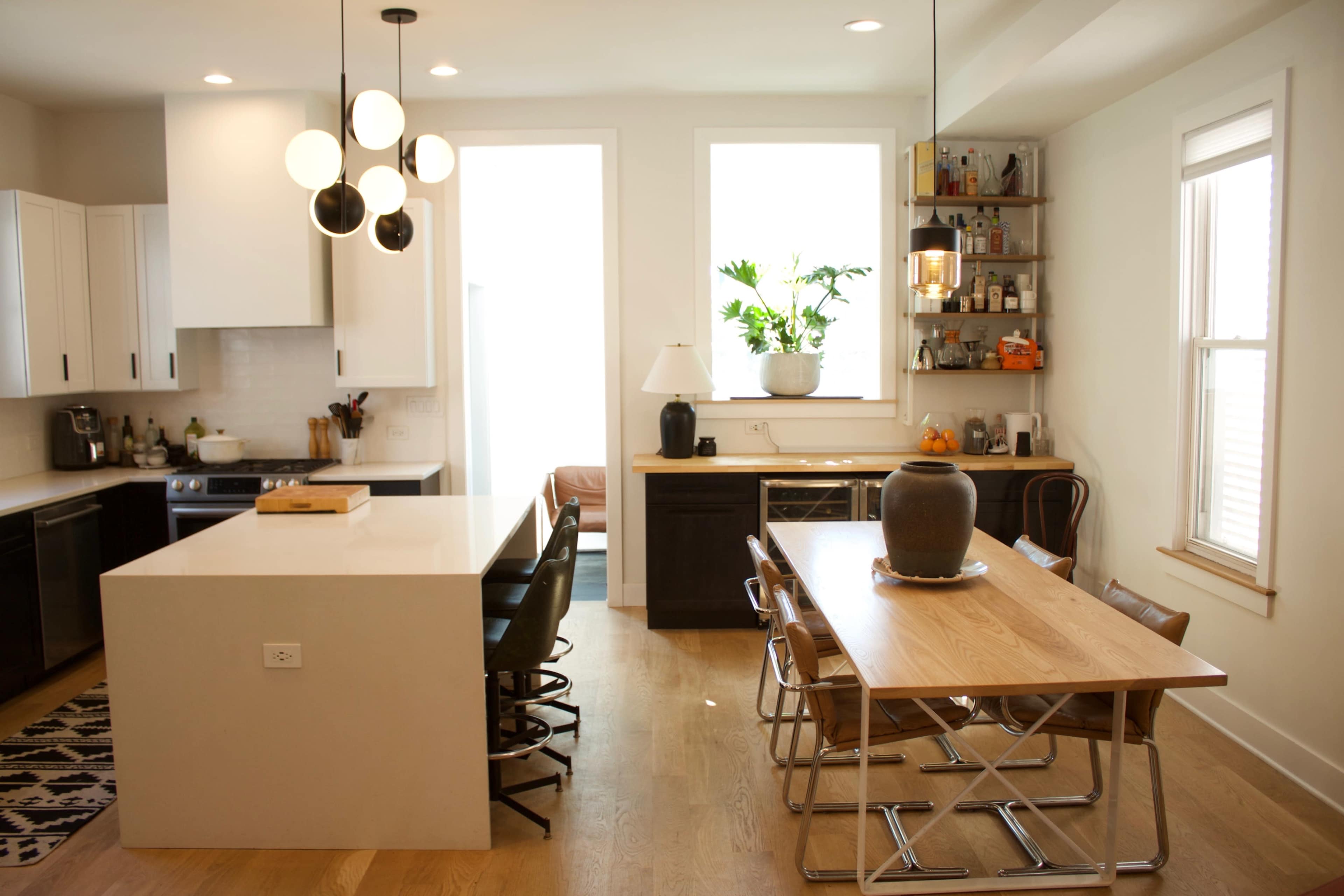 A modern kitchen features a large island with seating, a dining table, and natural light from large windows.