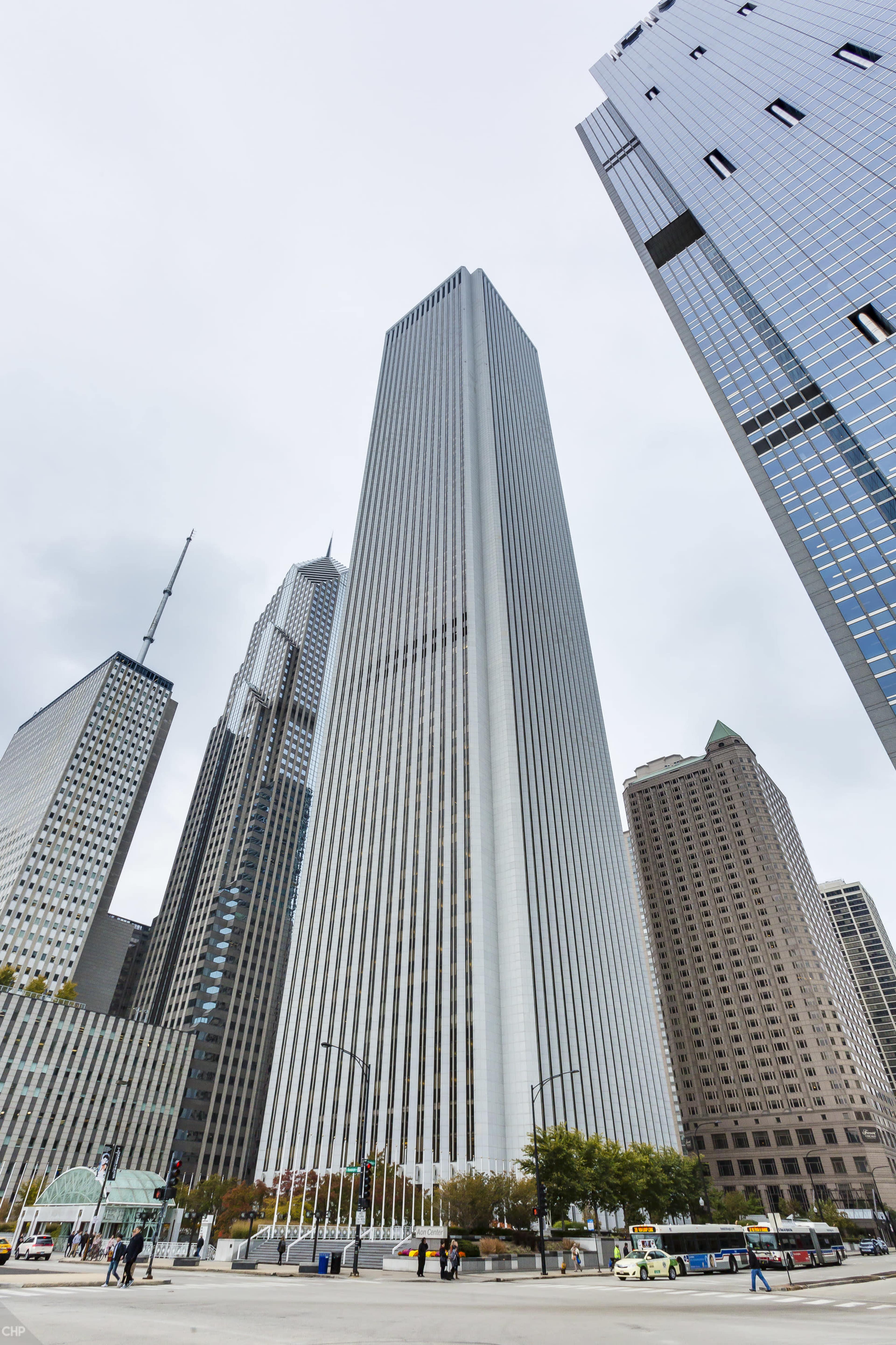 A tall skyscraper with vertical stripes stands among other buildings in a cityscape under an overcast sky.