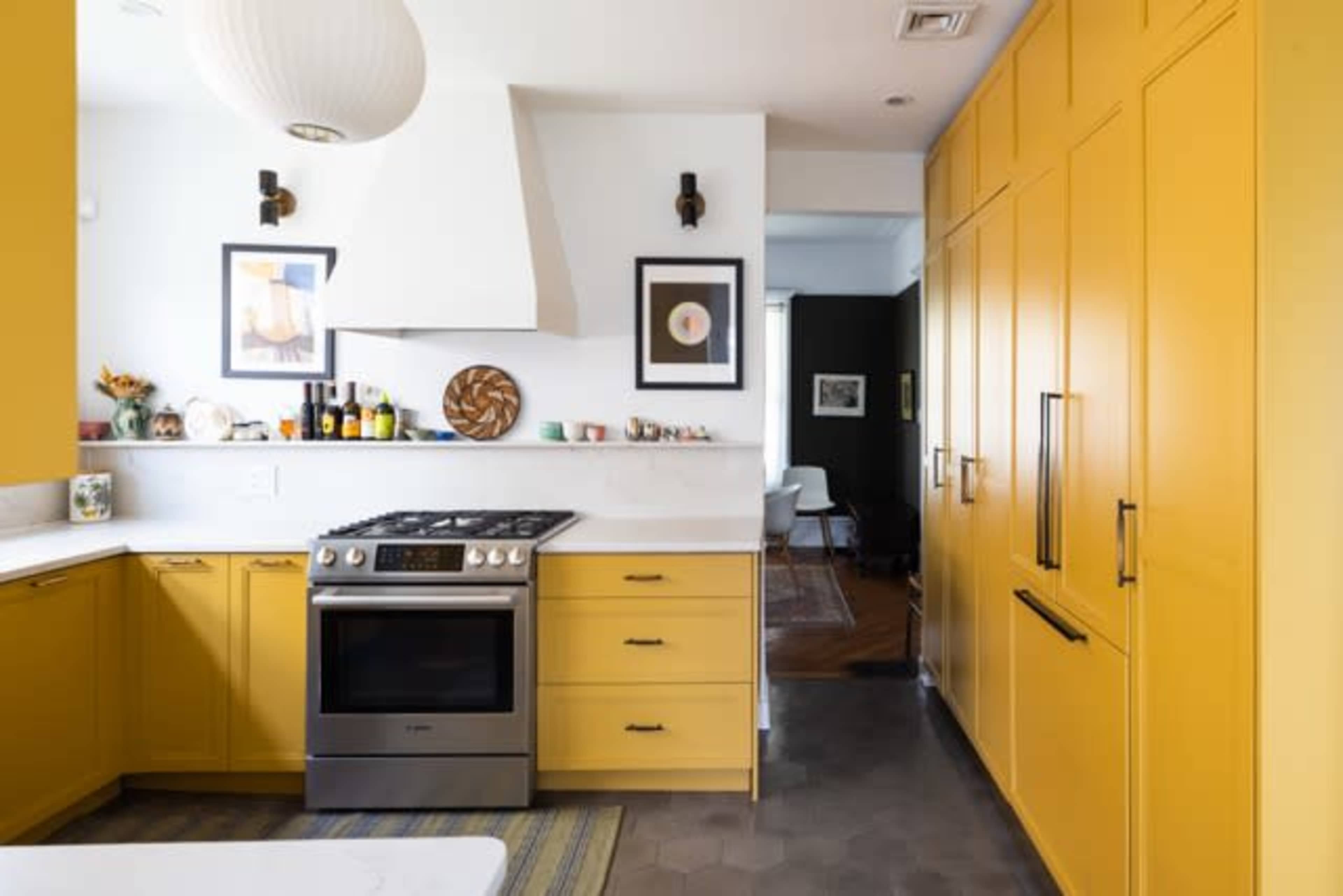 The image shows a modern kitchen with yellow cabinetry, a stainless steel stove, and marble countertops.