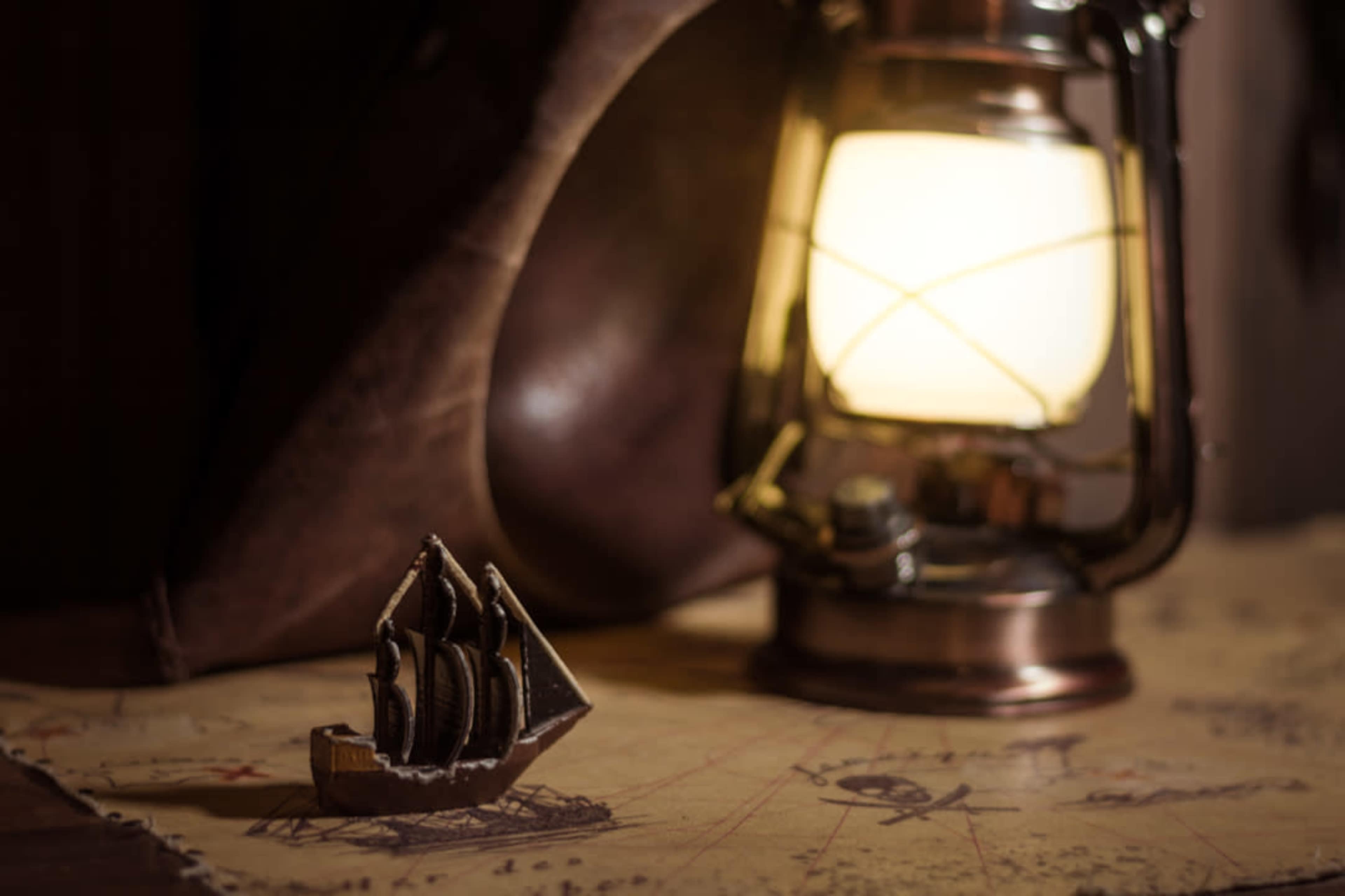 A small ship model rests on an old map beside an antique lantern.
