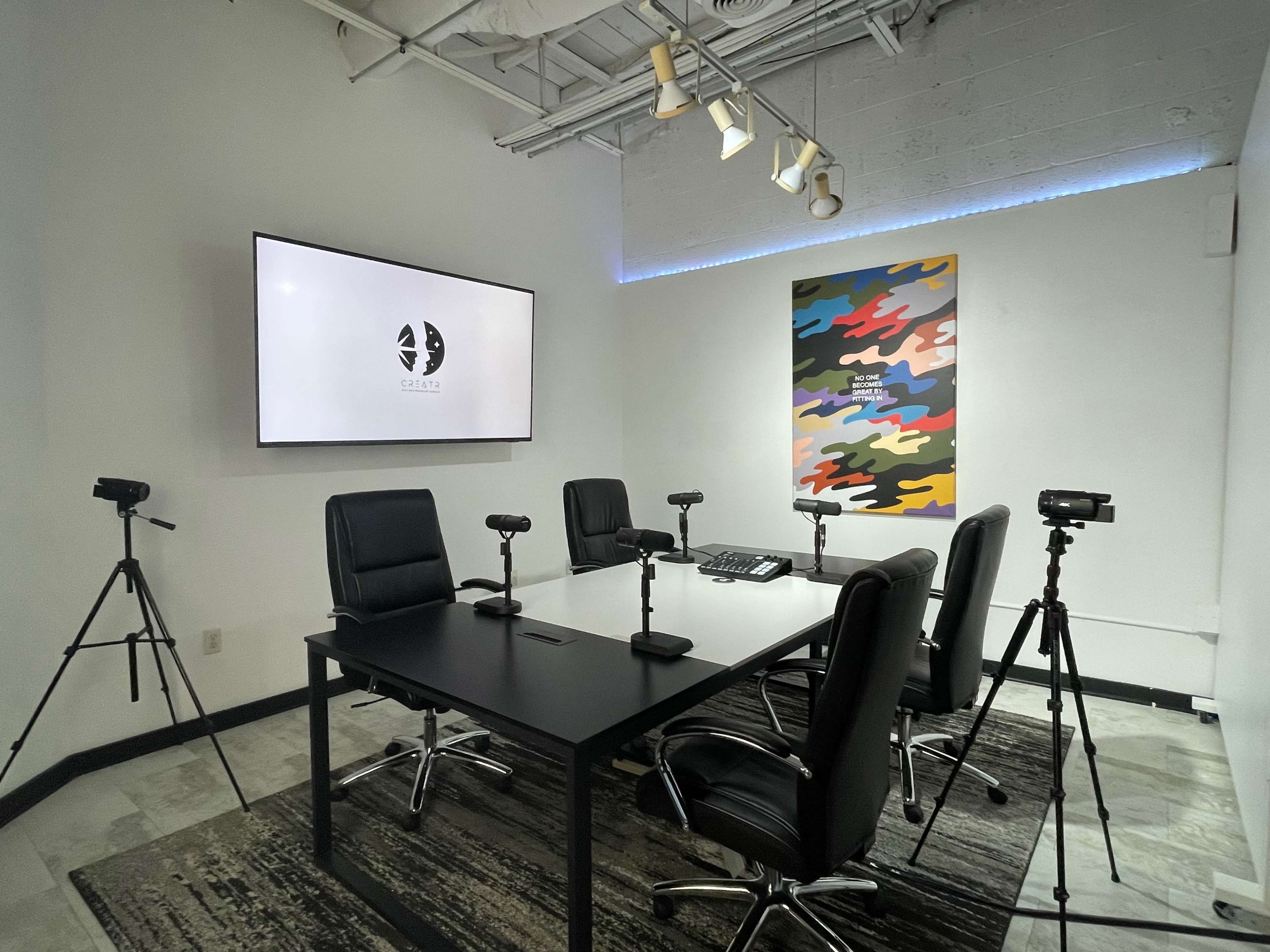 A modern conference room features a large display screen, a central table with chairs, and several cameras positioned on tripods.