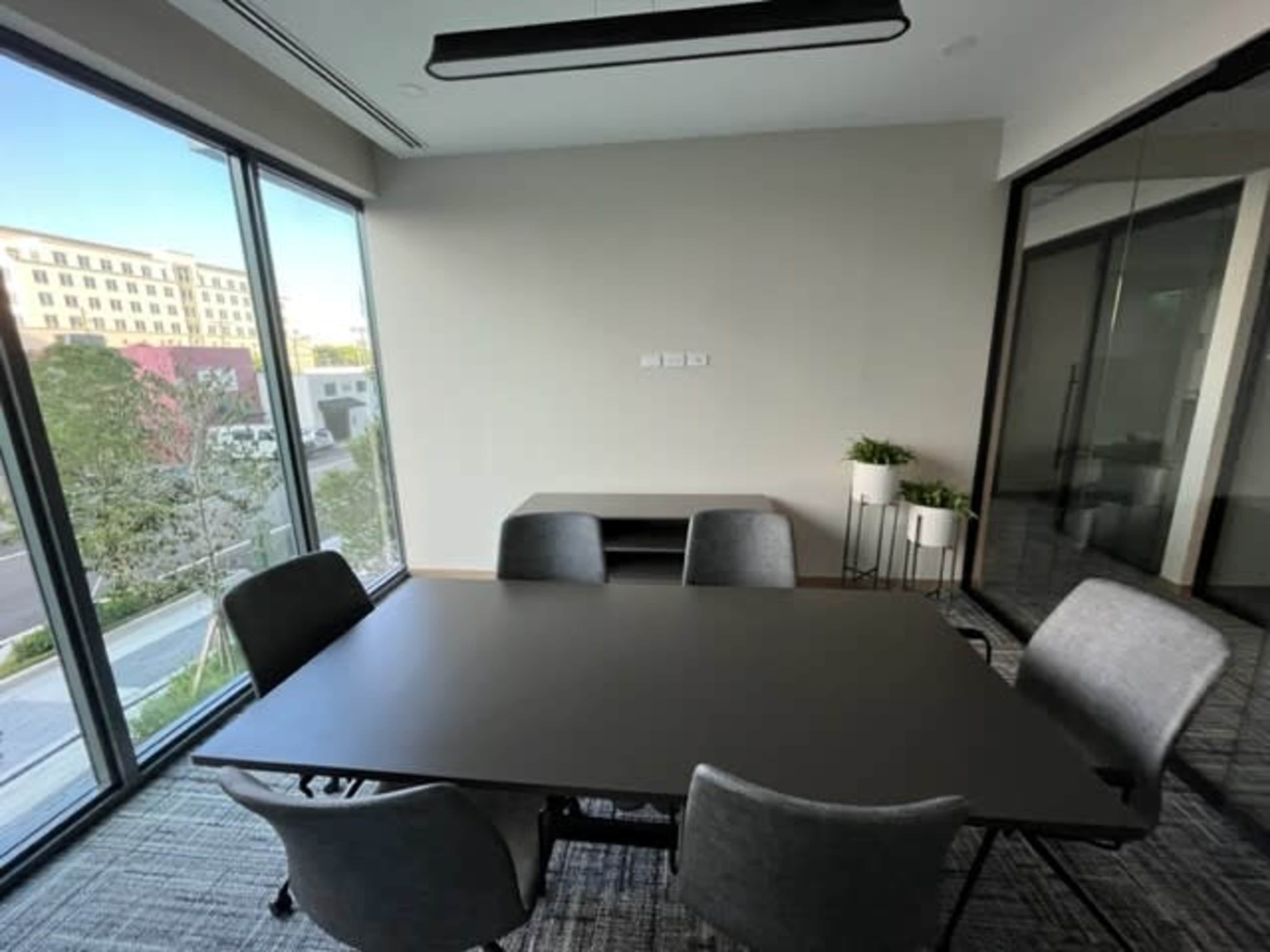 The image shows a modern conference room with a black table surrounded by gray chairs and large windows providing a view of the outdoors.