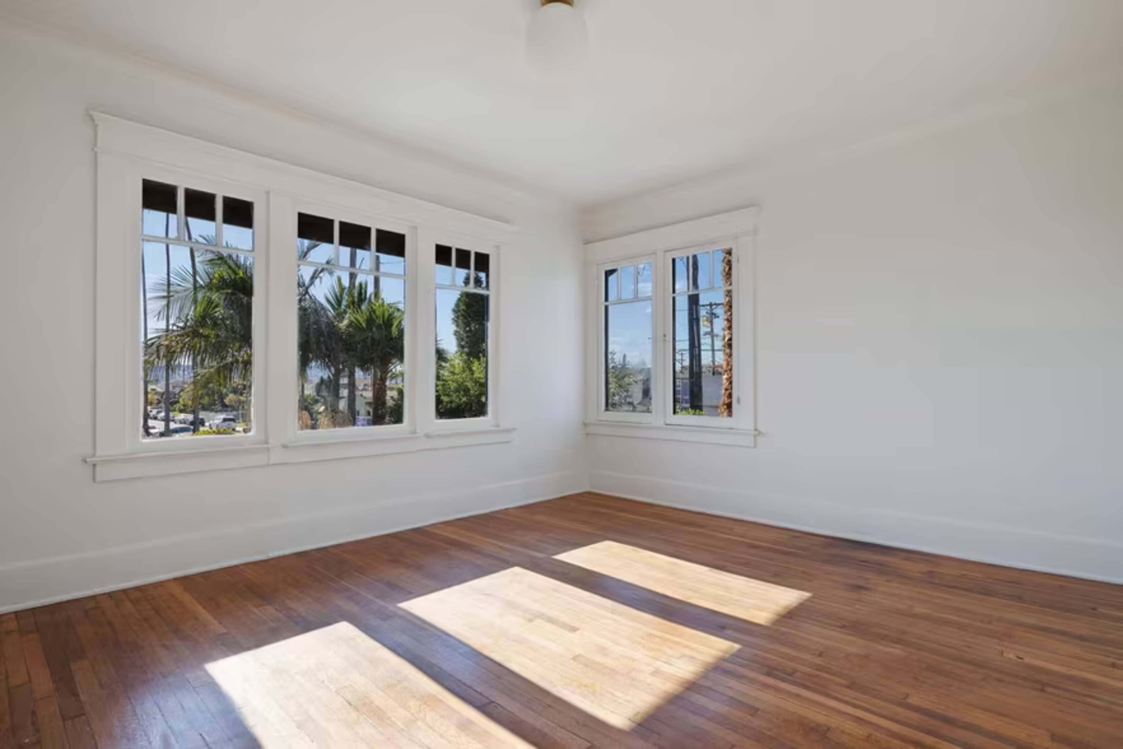 A bright and empty room with hardwood floors and large windows allowing natural light to enter.