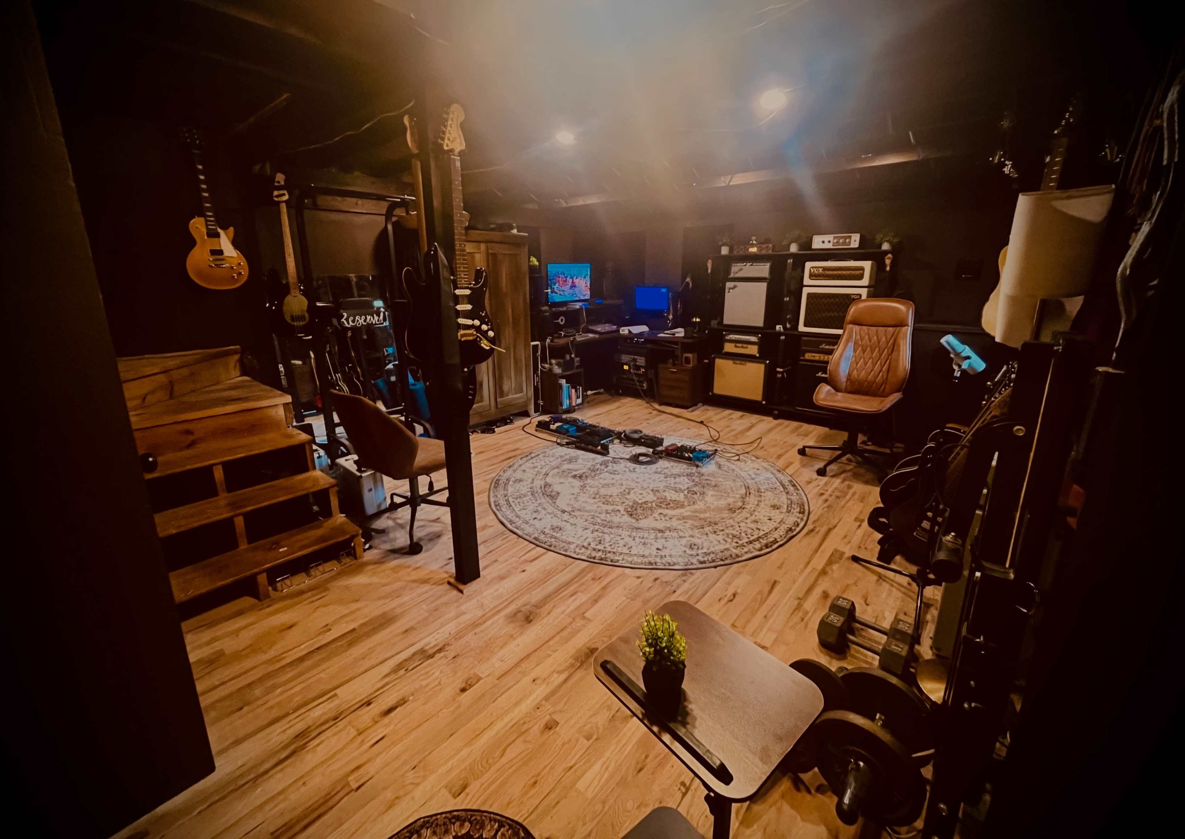 The image shows a dimly lit basement music studio with wooden flooring, various musical instruments, a television, and a cozy seating area.