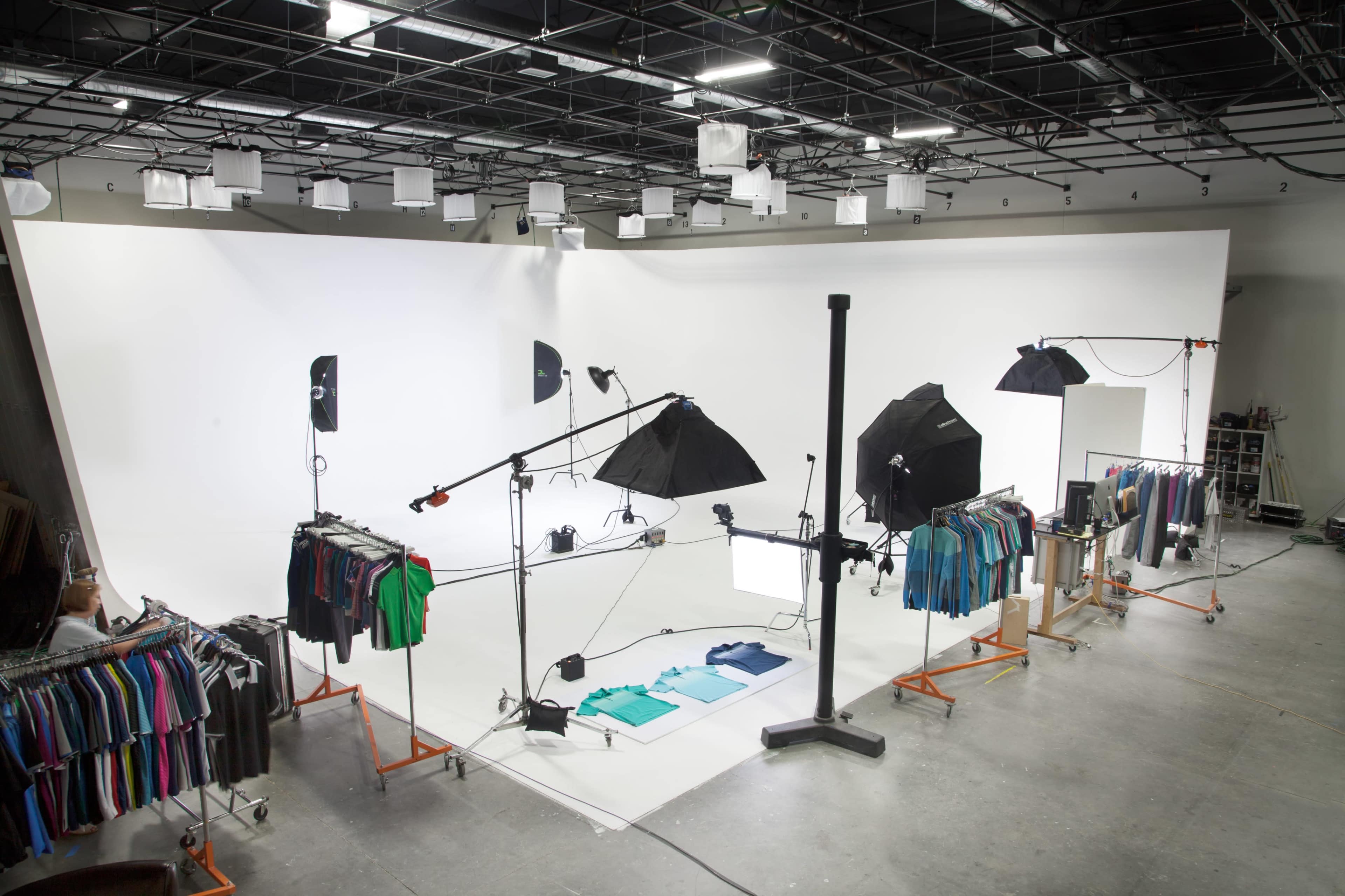 A photography studio setup with a backdrop, multiple lighting rigs, and clothing displayed on racks.