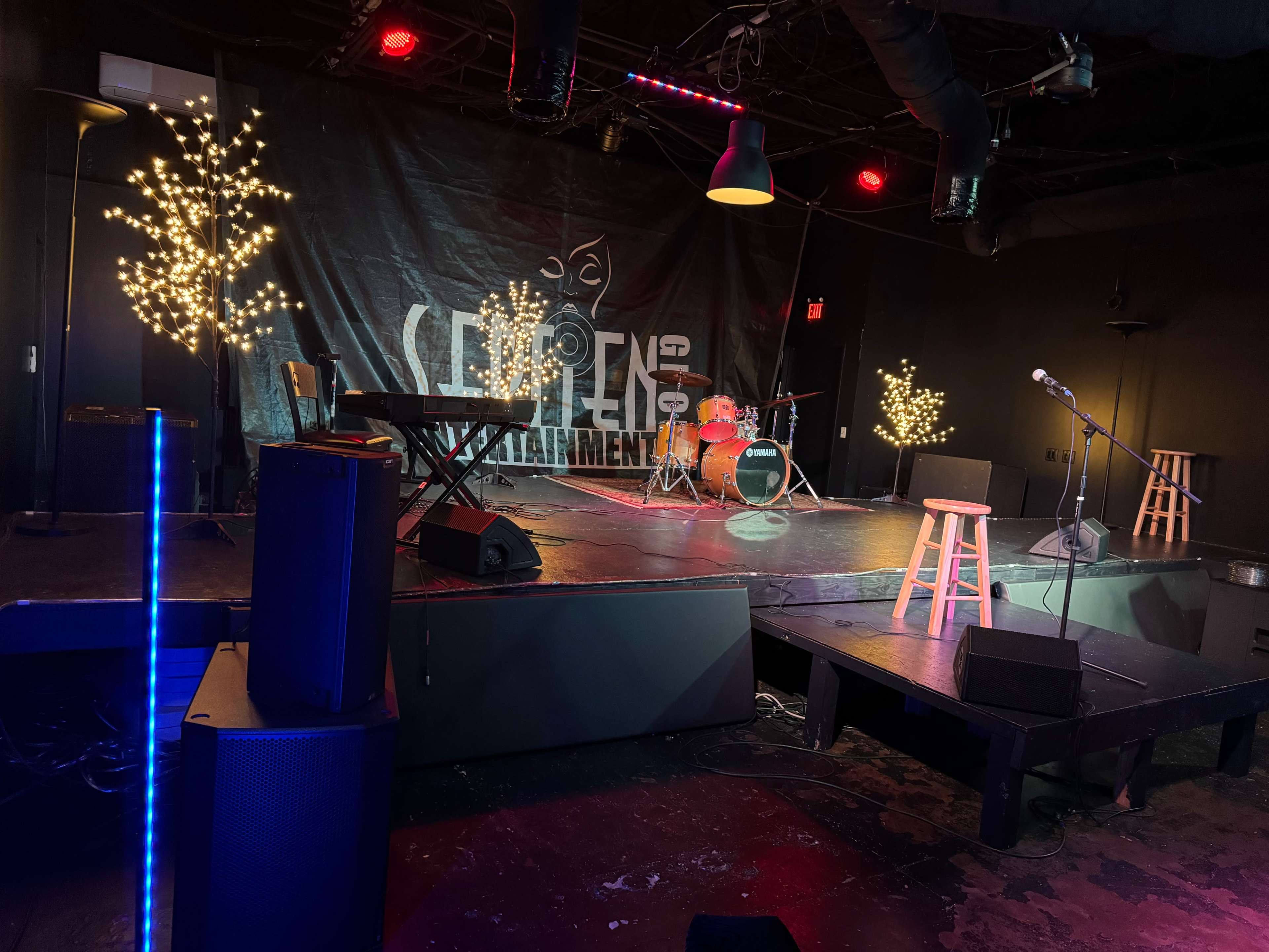 A small stage setup for a performance, featuring musical instruments, a microphone stand, and decorative lights in the background.