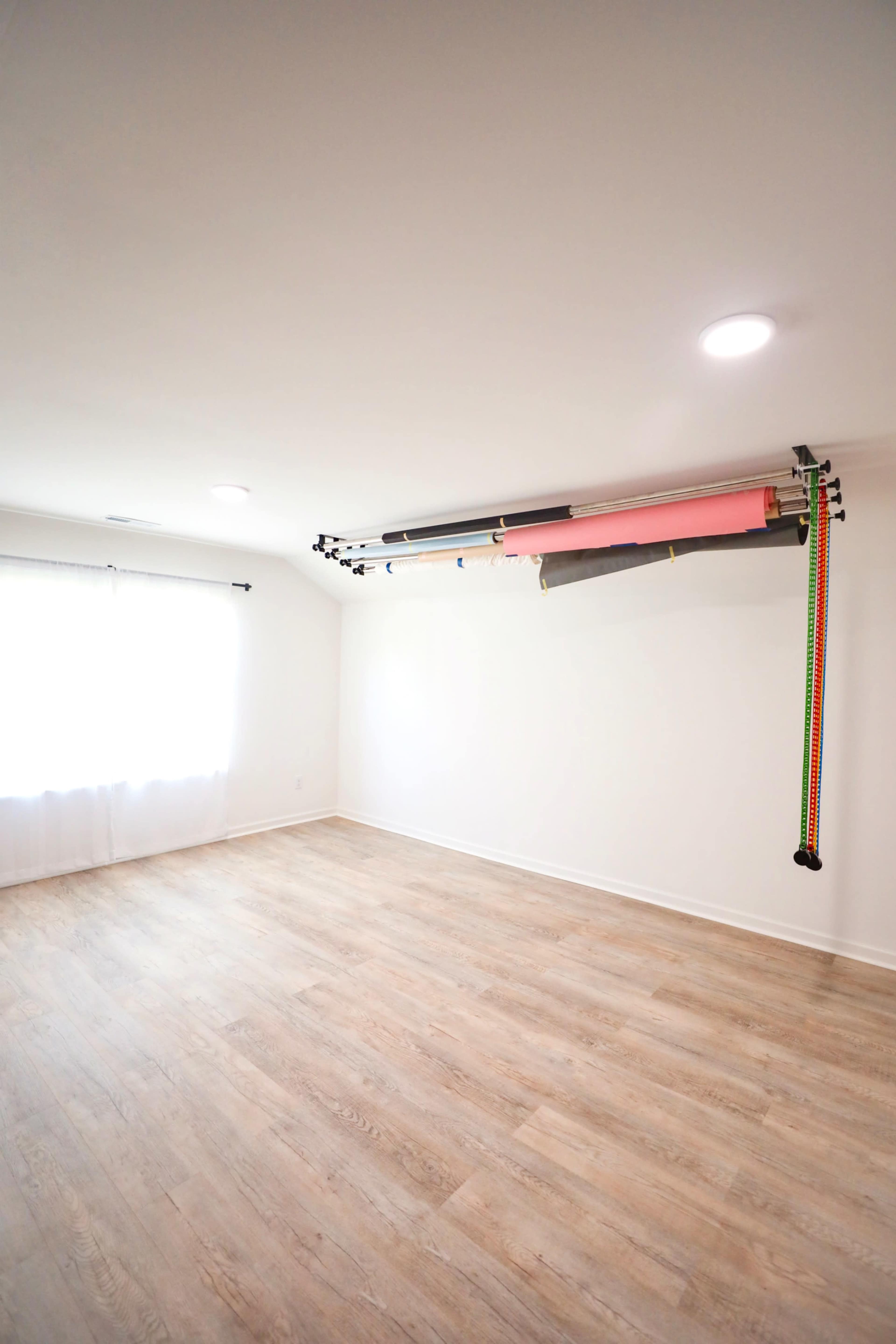 A brightly lit room features a wooden floor and a backdrop support system mounted on the wall, holding various colored backdrops.