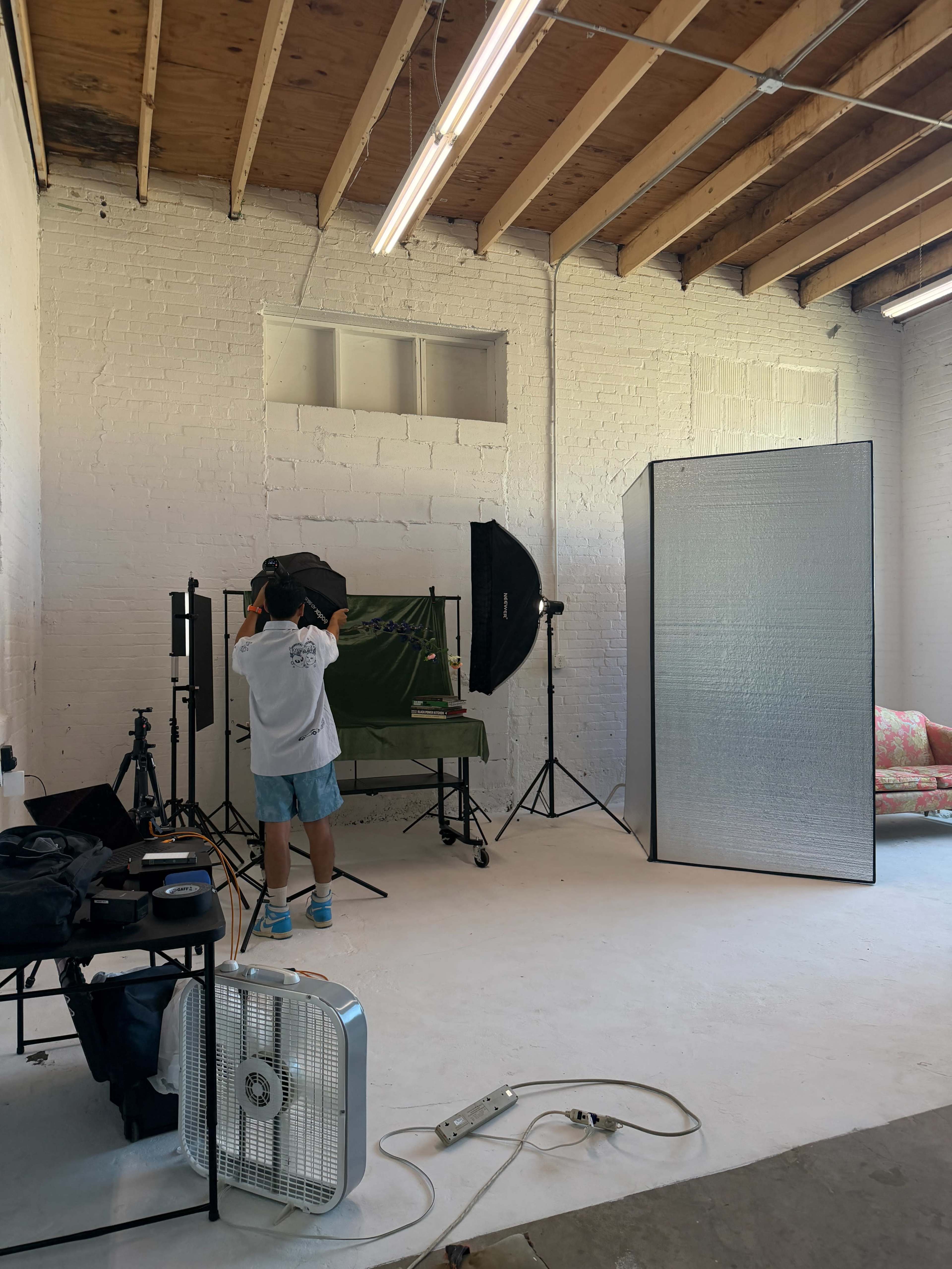 A person adjusts lighting equipment in a photography studio with a green backdrop and a large reflective screen.