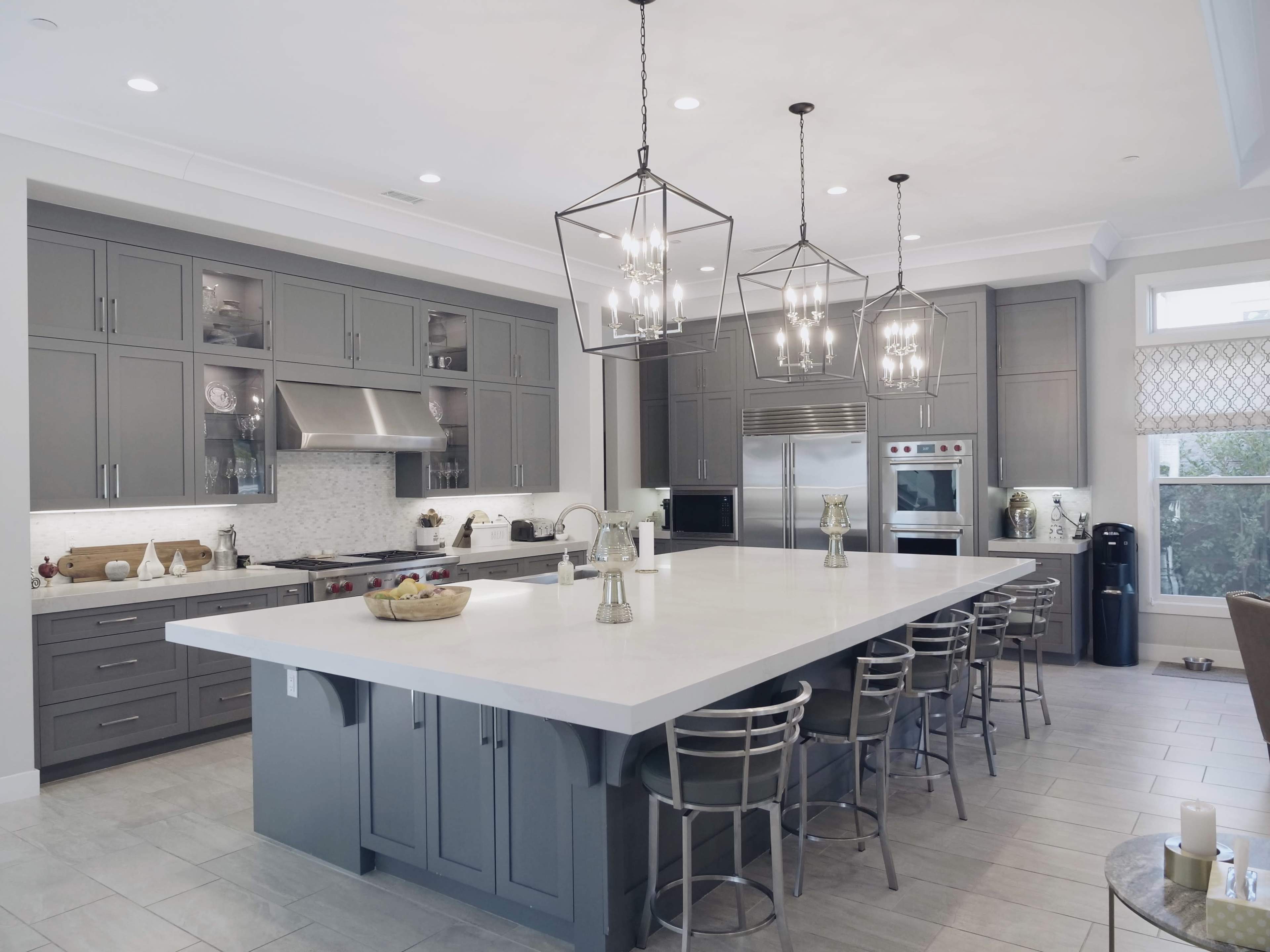 The image shows a modern kitchen featuring gray cabinetry, a large island with seating, and pendant lighting.