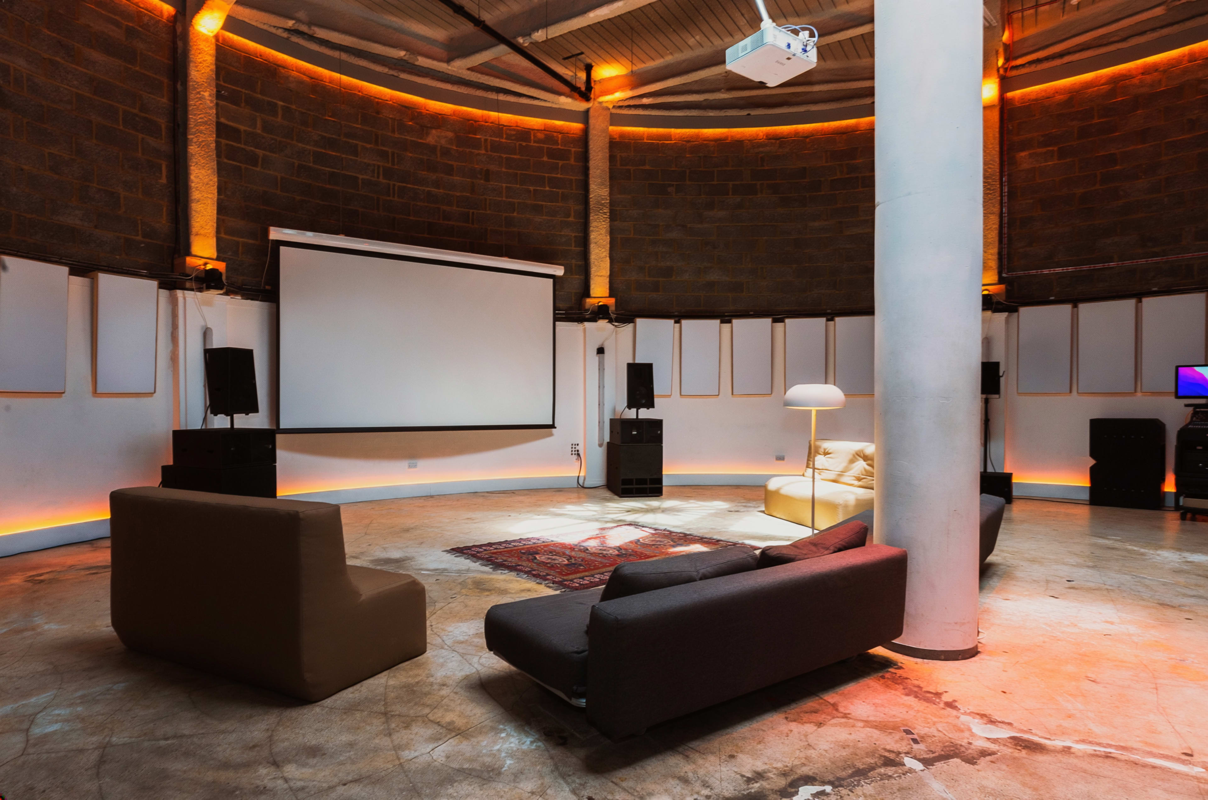 The image shows a circular home theater room with a large screen, projector, and various seating options arranged around a central area.