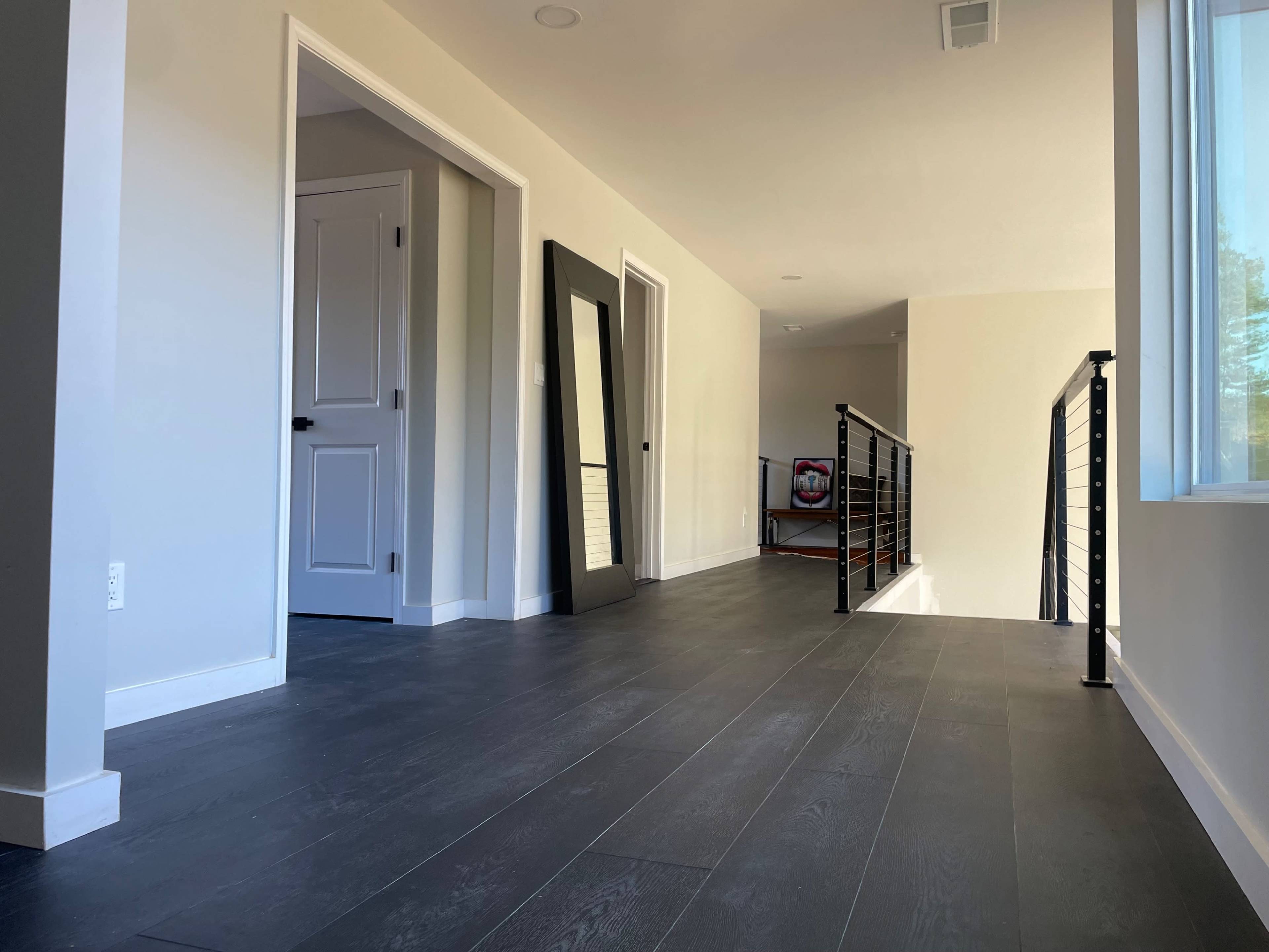 The image shows a modern hallway with hardwood flooring, a large mirror against the wall, and multiple doors leading to other rooms.