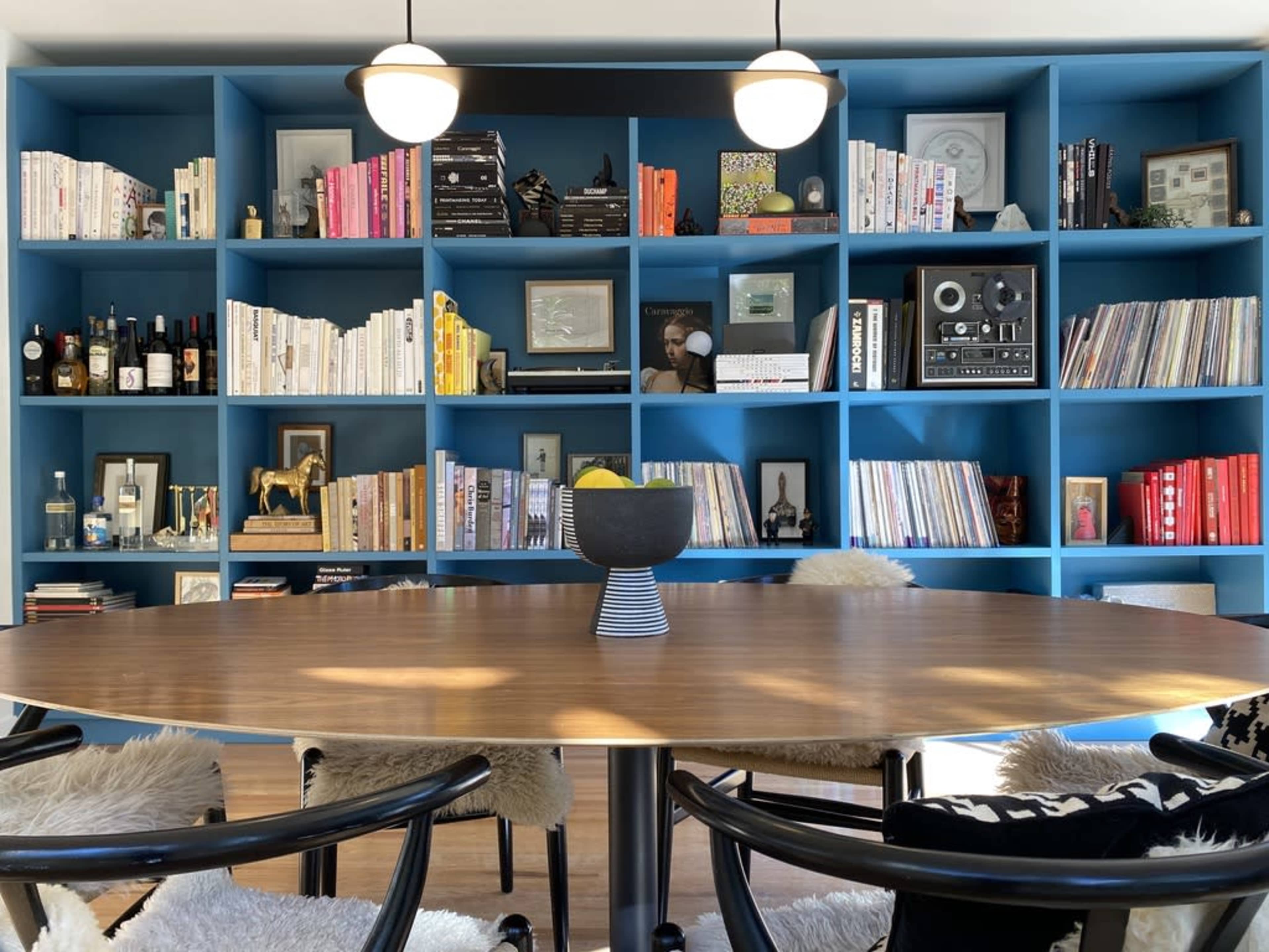 A round wooden table is positioned in front of a blue bookshelf filled with books, photographs, and decorative items.
