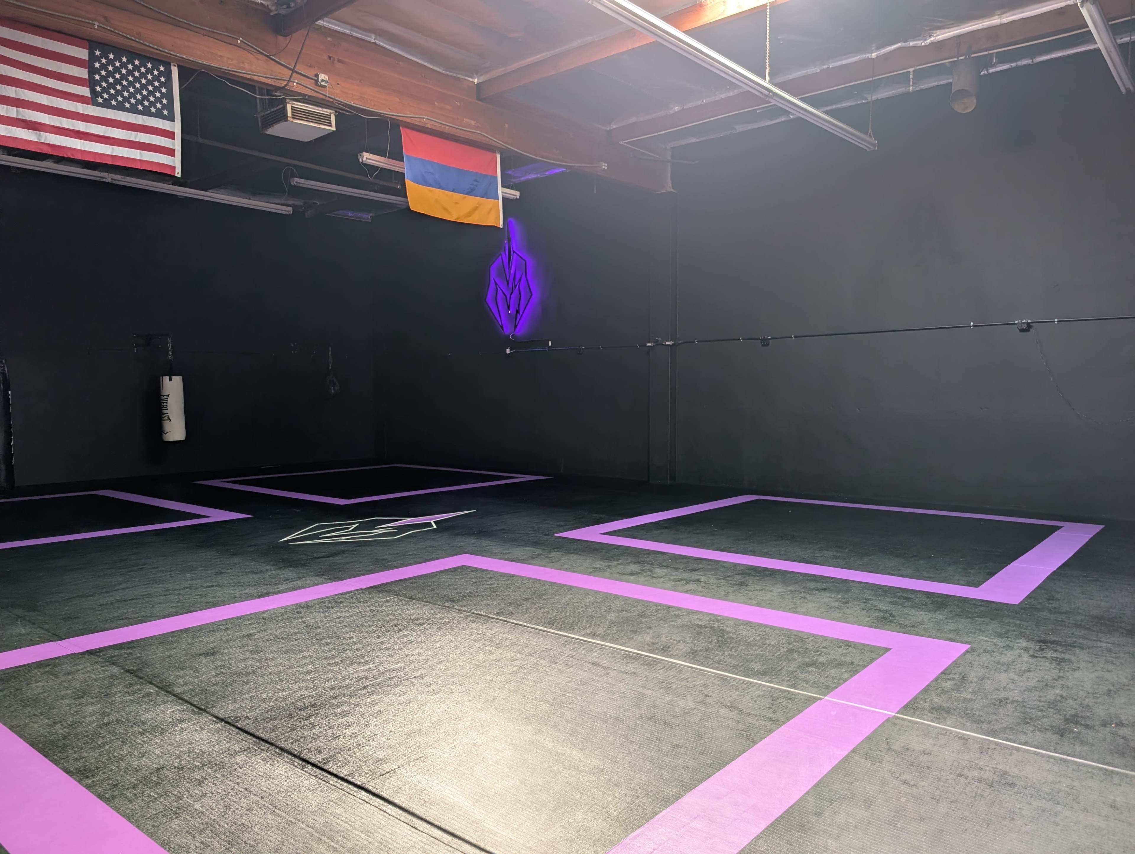The image shows a sparsely furnished training space with a black floor and purple markings, featuring an American flag and an Armenian flag hanging from the ceiling.