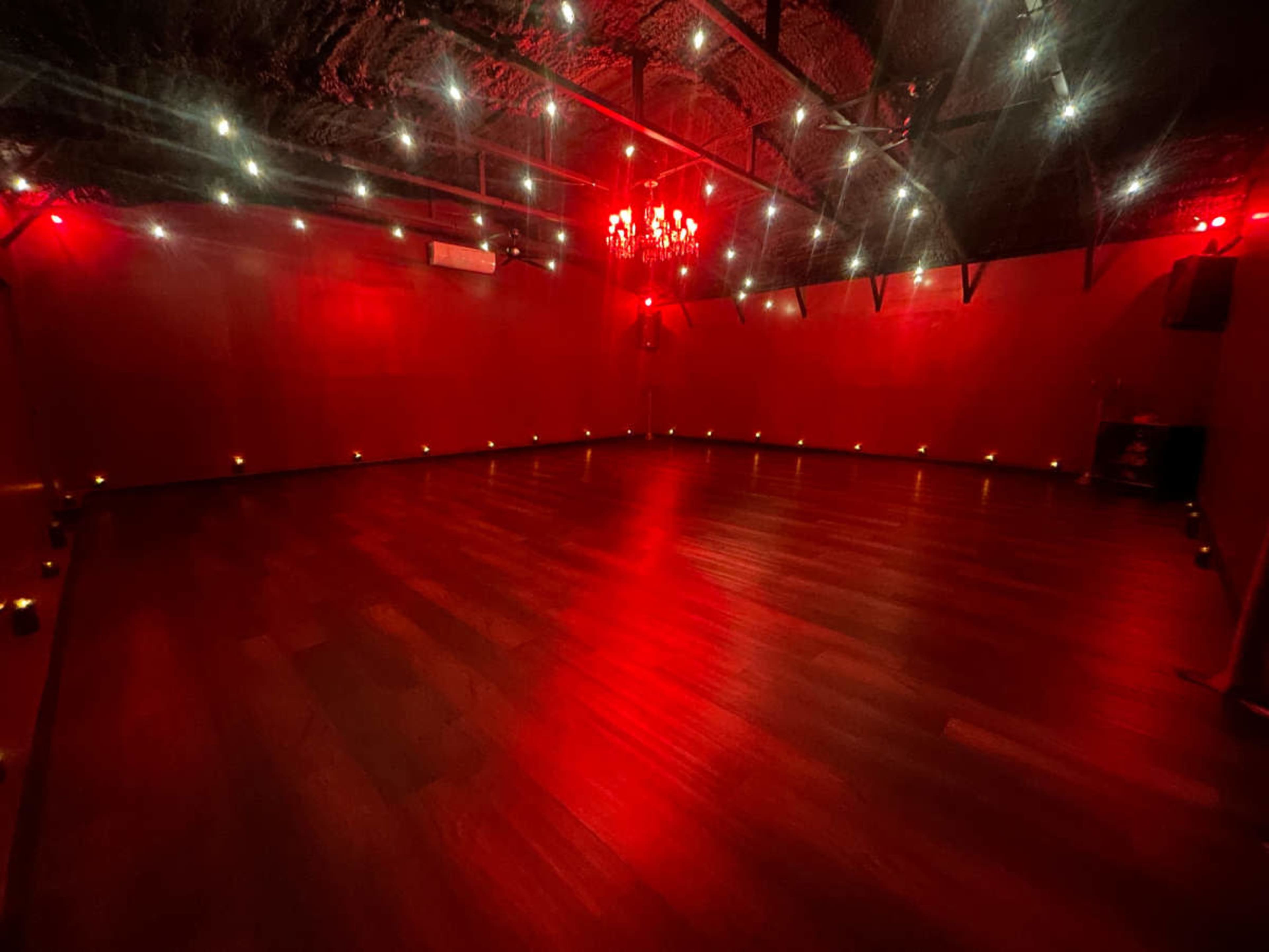 The image shows a dimly lit room with red walls, ambient lighting from candles around the perimeter, and a chandelier hanging from the ceiling.