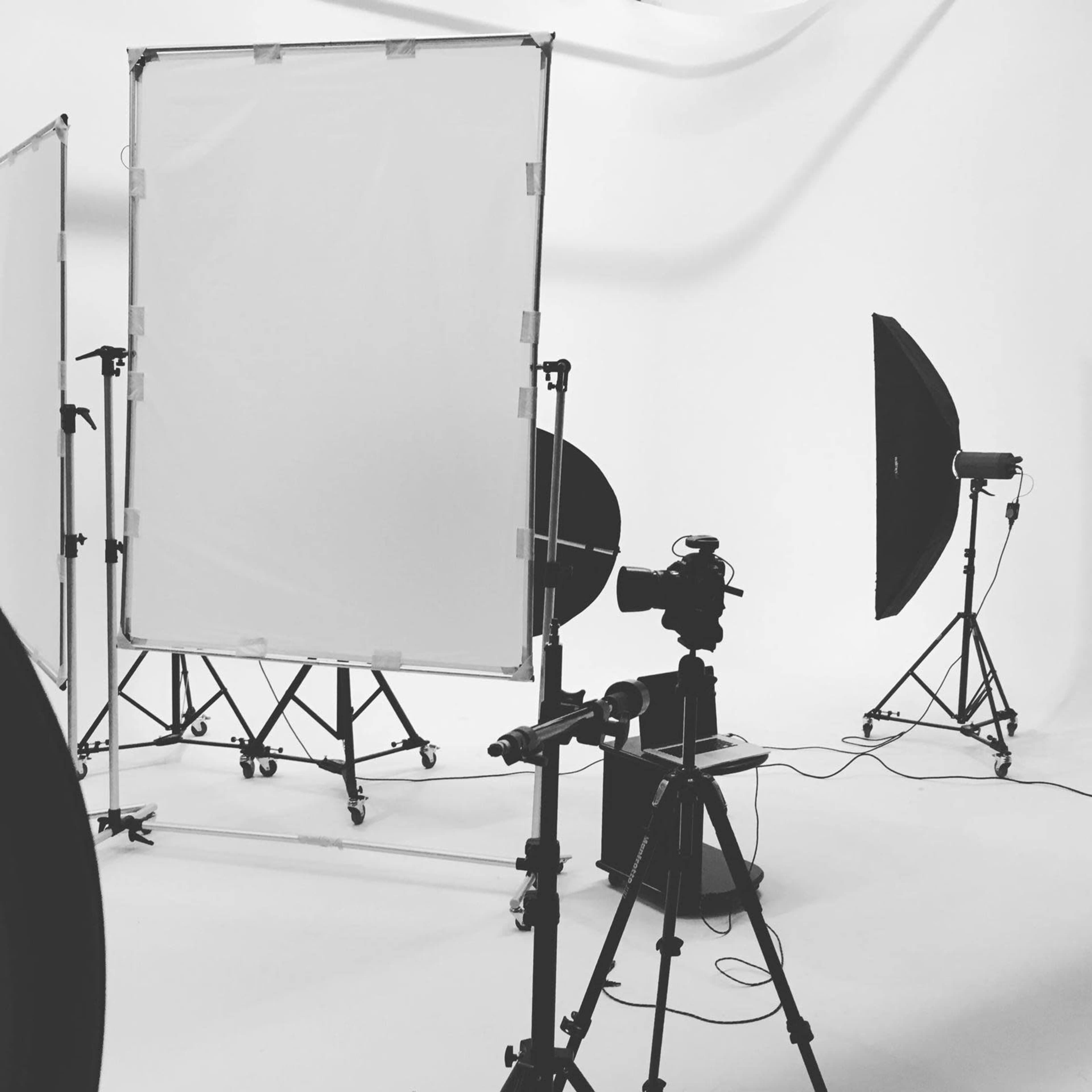 The image depicts a photography studio setup with a camera, lighting equipment, and blank backdrop screens.