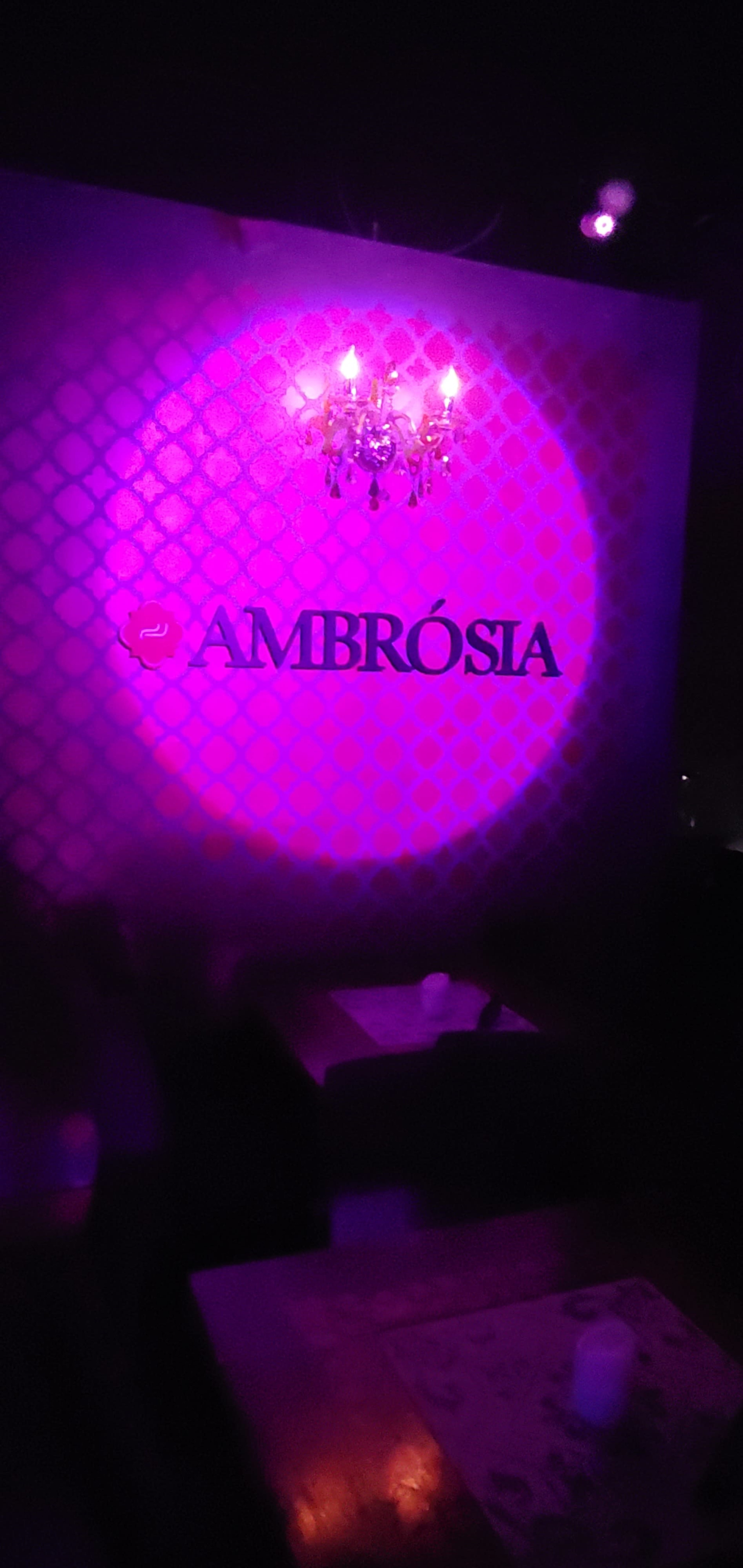 The image shows a dimly lit interior of a venue featuring a chandelier and a wall displaying the name "AMBROSÍA" in a decorative font.