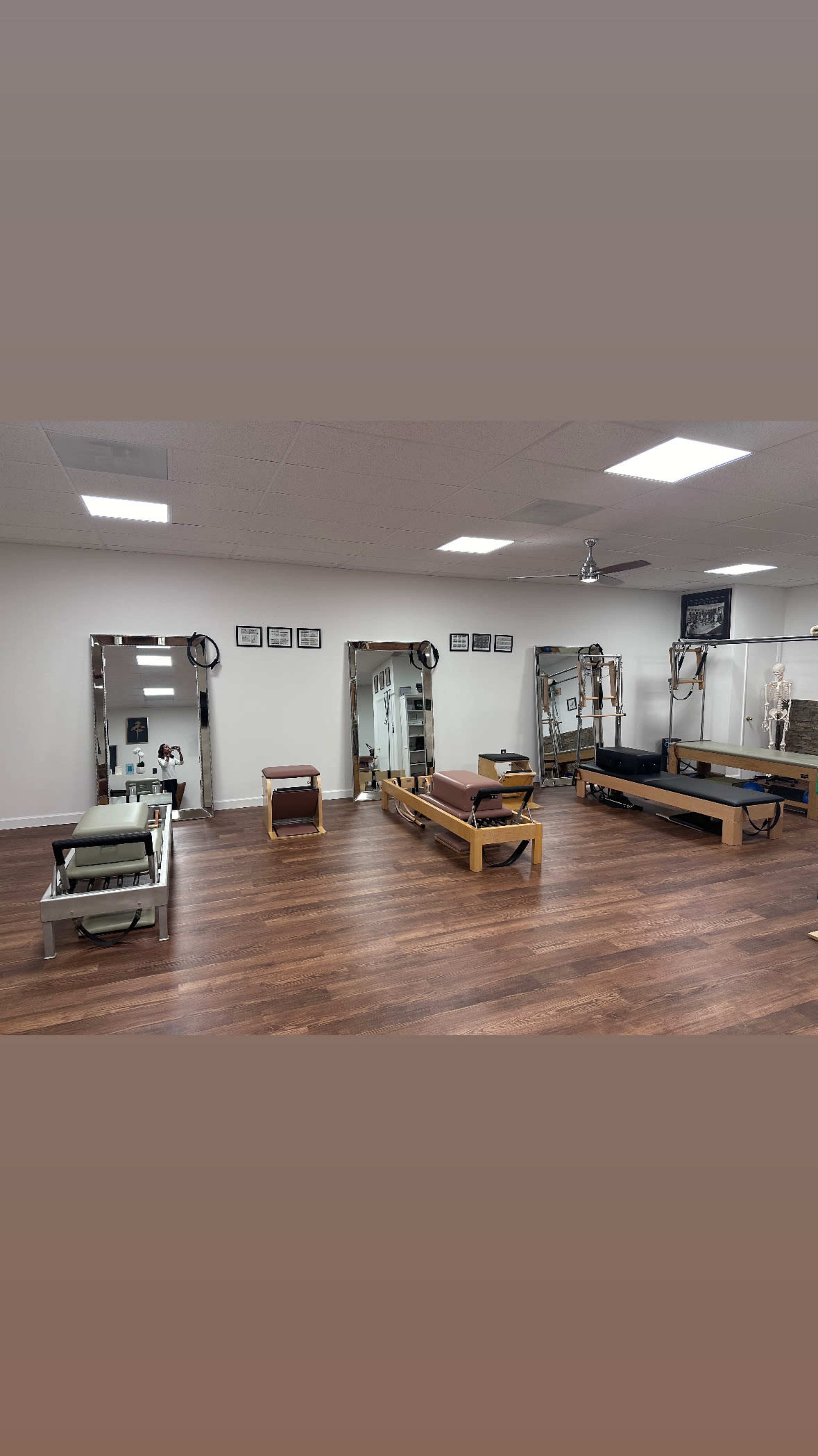 The image shows a pilates studio with several reformer machines arranged on a wooden floor and mirrors on the walls.