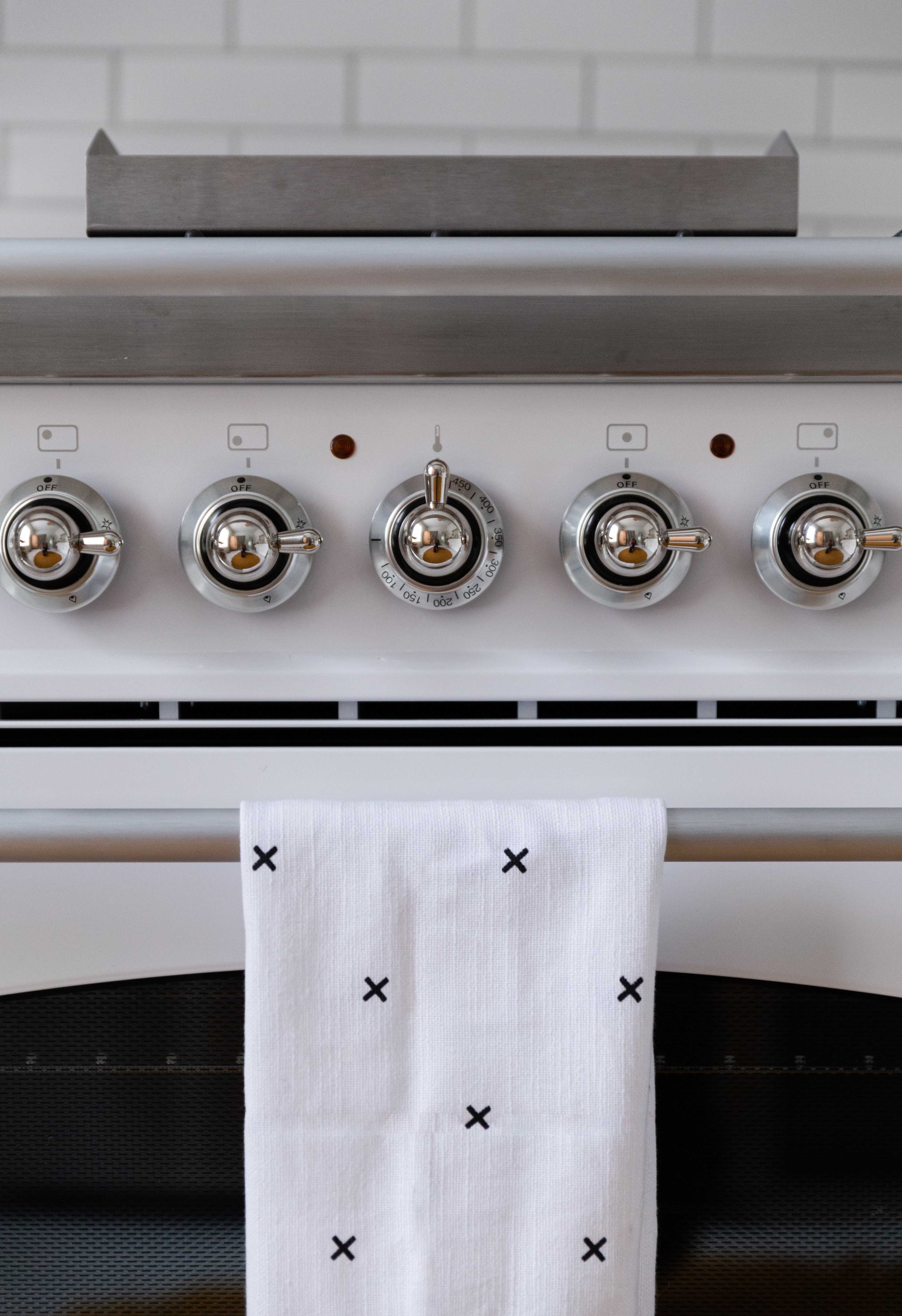 A close-up view of a modern kitchen stove with shiny knobs and a white towel hanging from the oven door.