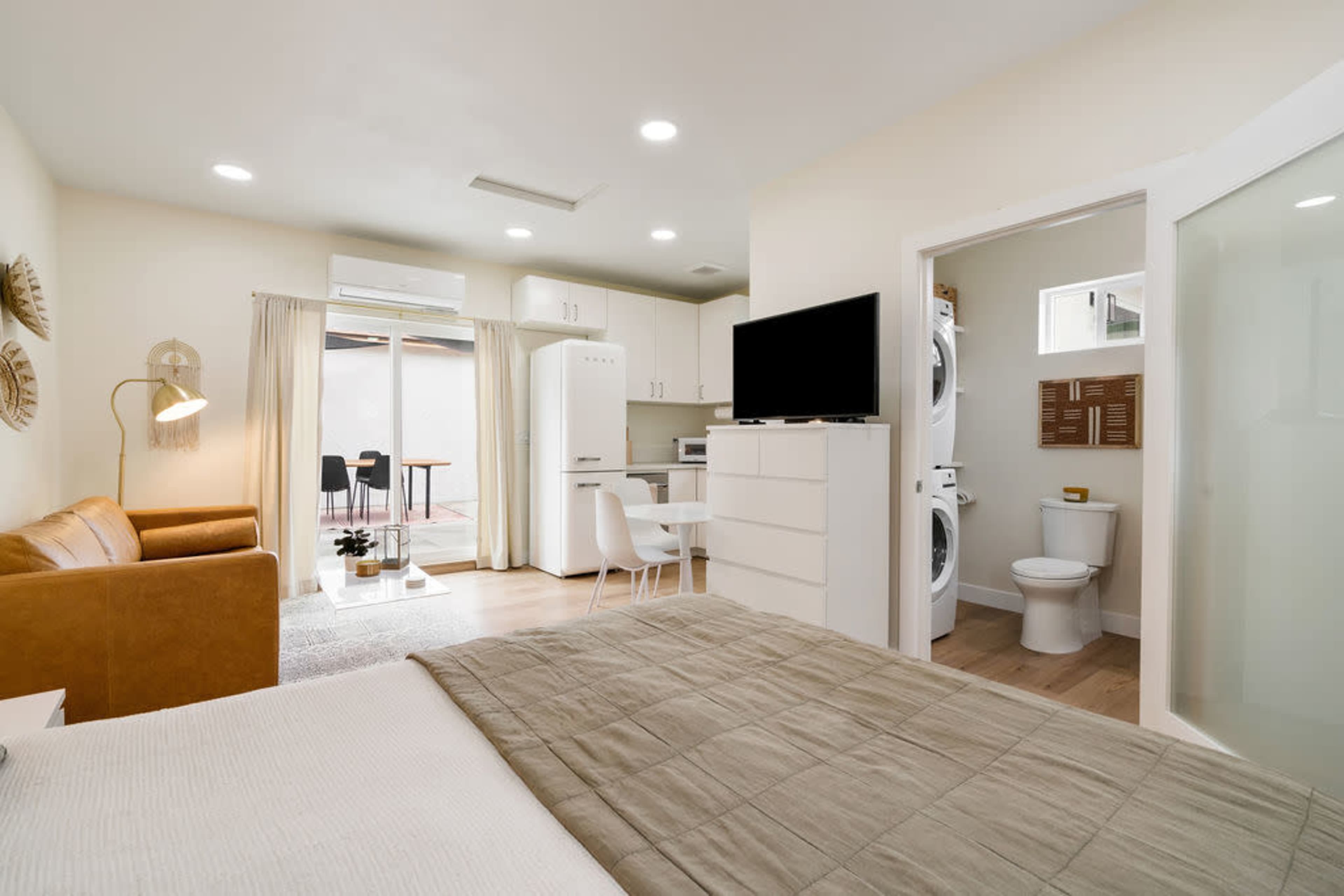 A compact living space features a bed, a seating area, a kitchen, and a bathroom with laundry facilities.