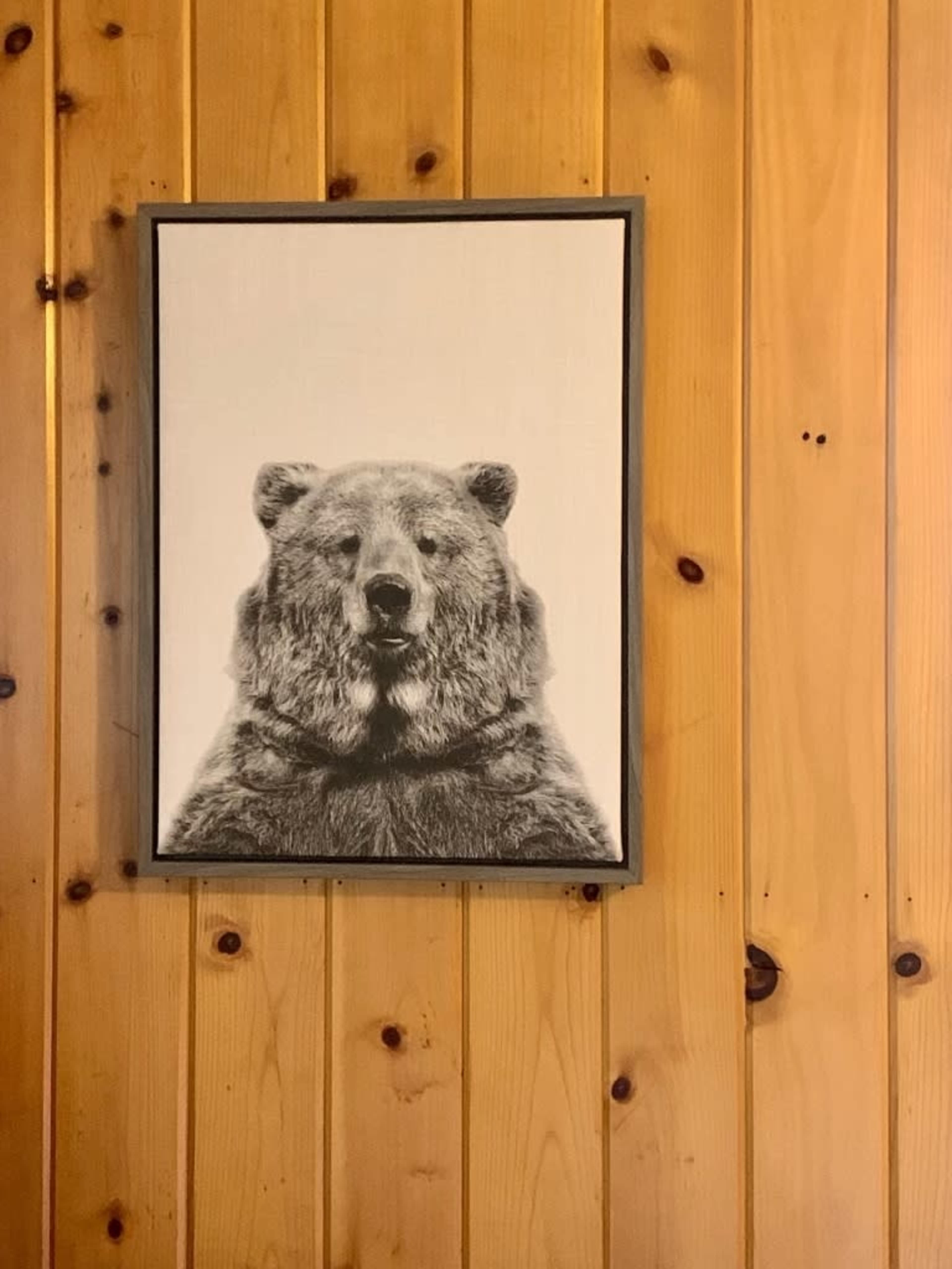 A framed black and white portrait of a bear hangs on a wooden wall.